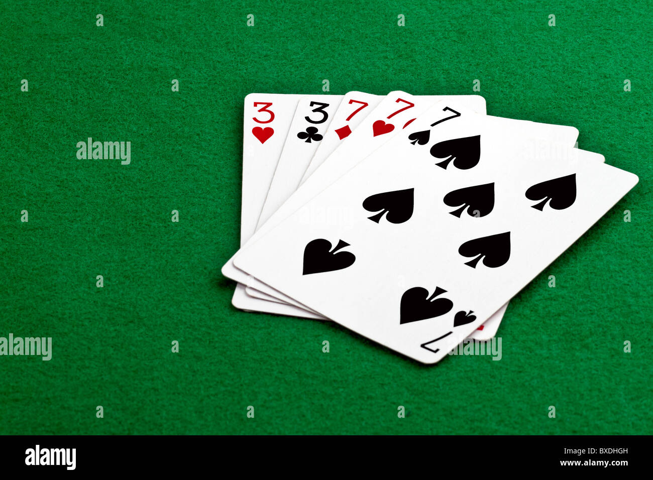 Poker hand full house with threes and sevens on green felt Stock Photo