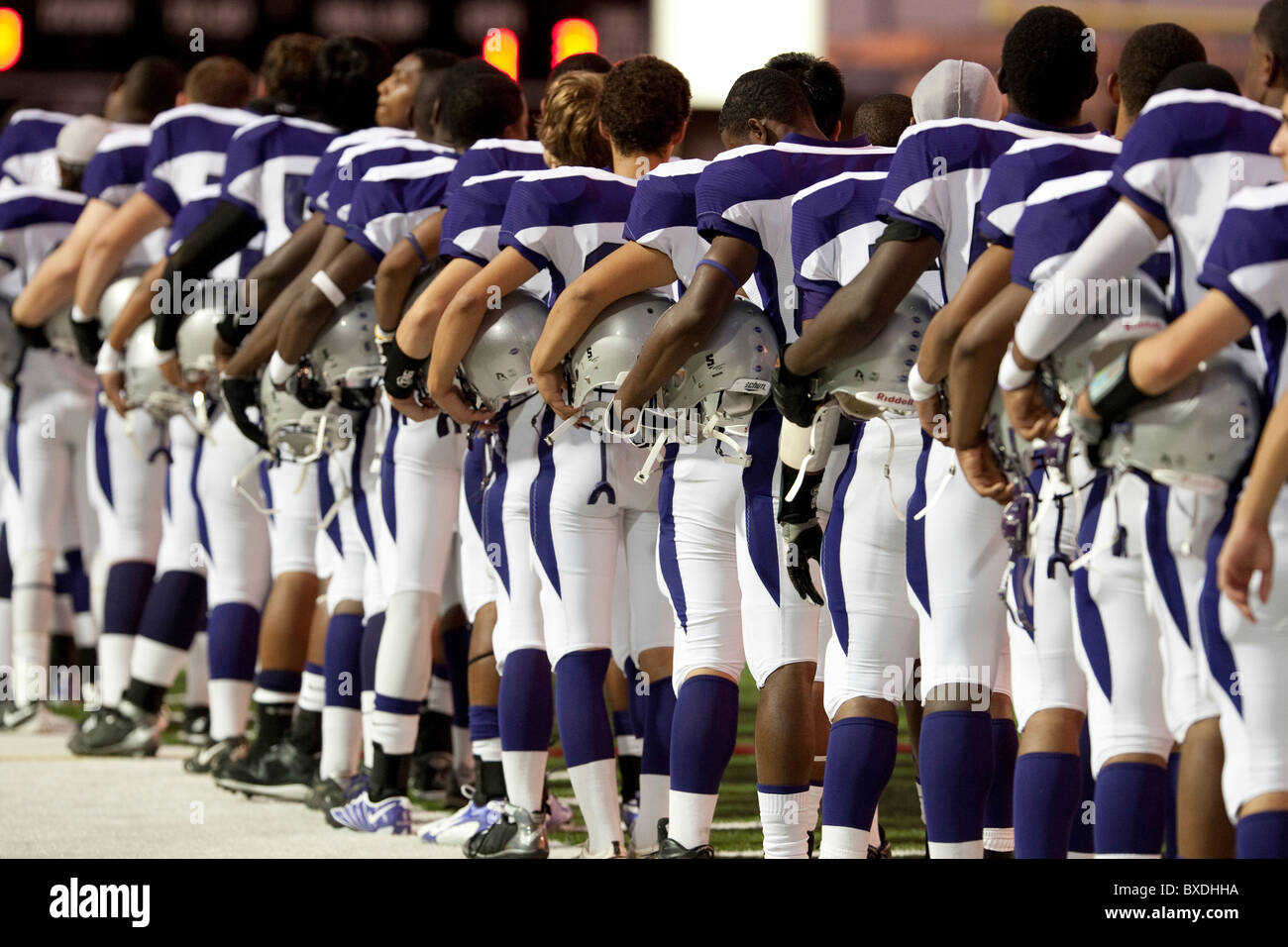 Football players hold their helmets on their hips while lined up before the game during the playing of the national anthem Stock Photo