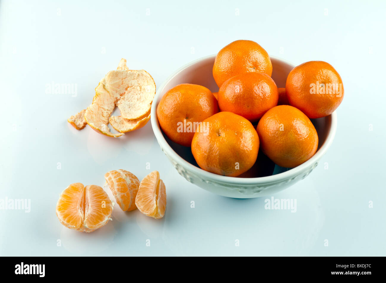 Peeled clementines and clementines in white bowl on white surface Stock