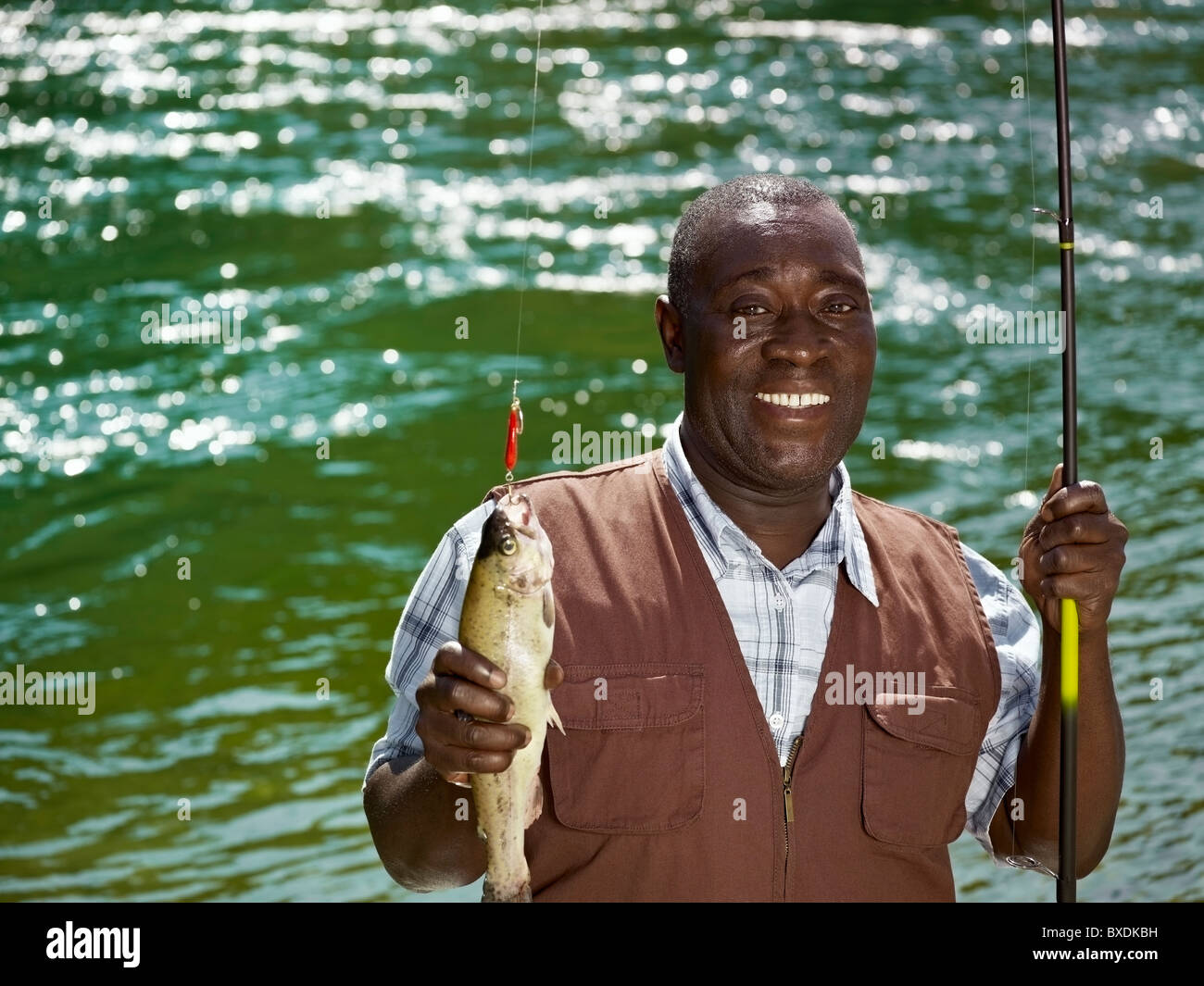 Black man holding fish and fishing rod near stream Stock Photo - Alamy
