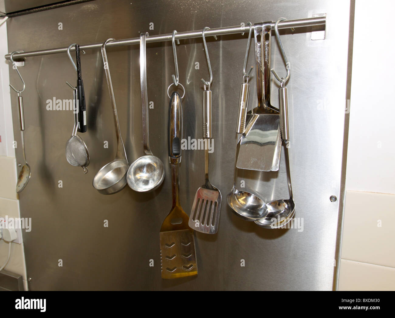 Cooking utensils hanging on rail in commercial kitchen Stock Photo