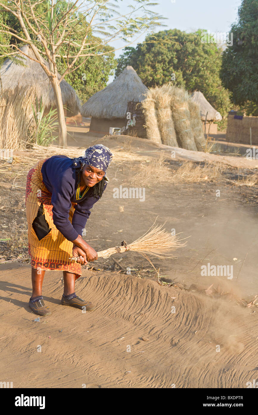 Young woman sweeps ground with a straw broom in her village. Zambia