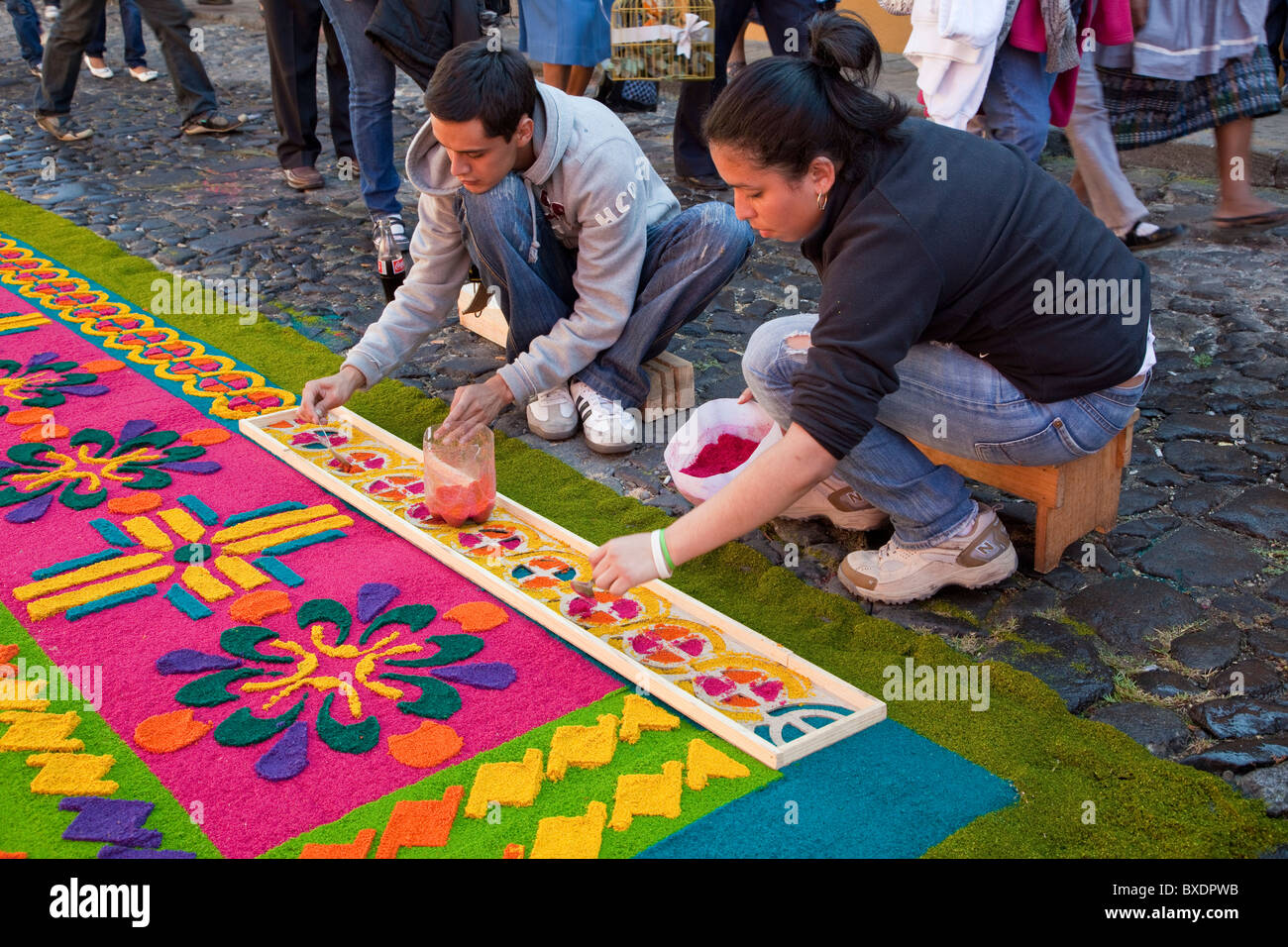 Antigua, Guatemala. Using a stencil to put finishing touches on an alfombra (carpet) of colored sawdust awaiting a procession. Stock Photo