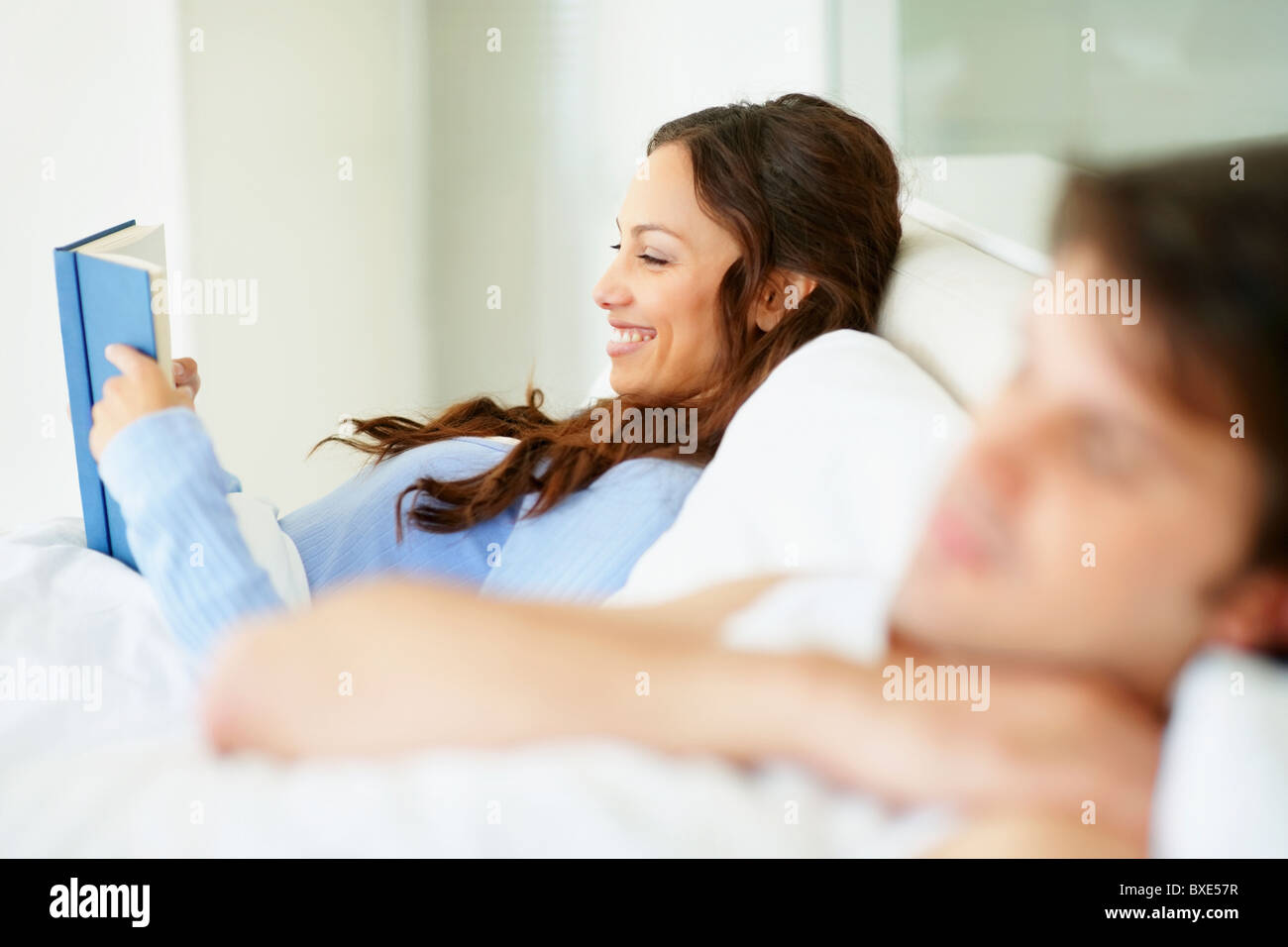 Woman reading book in bed beside sleeping husband Stock Photo Alamy