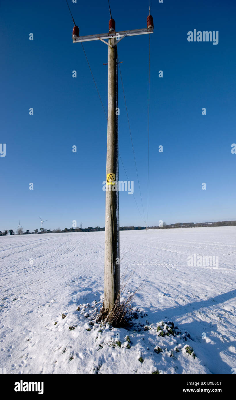 Single telegraph pole with a danger of death sign on it.  Alone in a snow covered field with a deep blue winter sky. Stock Photo
