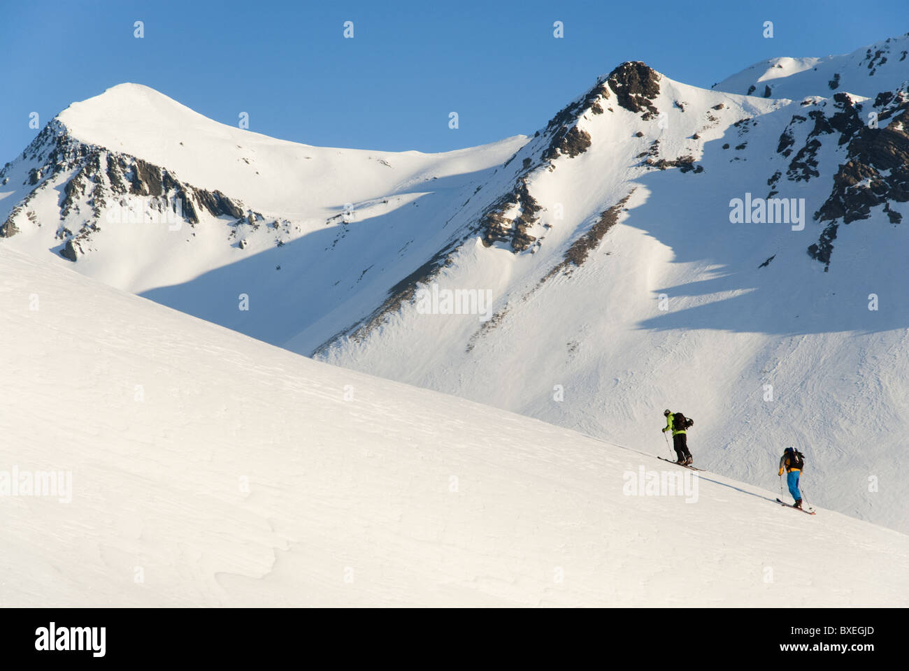 Two men climbing up a snowy mountain side with climbing skins on their skis at Col du Lautaret, near La Grave, France. Stock Photo