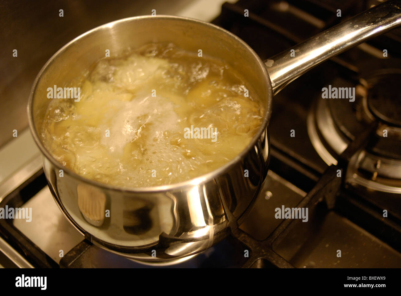 Potatoes simmering in a pan of boiling water on a gas hob. Stock Photo
