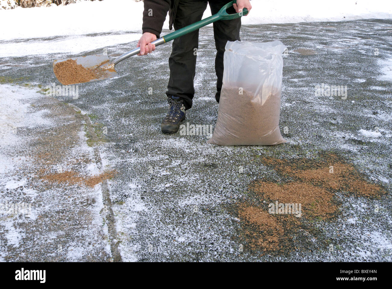Caucasian Man Applying Rock Salt ( Gritting ) to an Icy Path and Driveway, UK MODEL RELEASED Stock Photo
