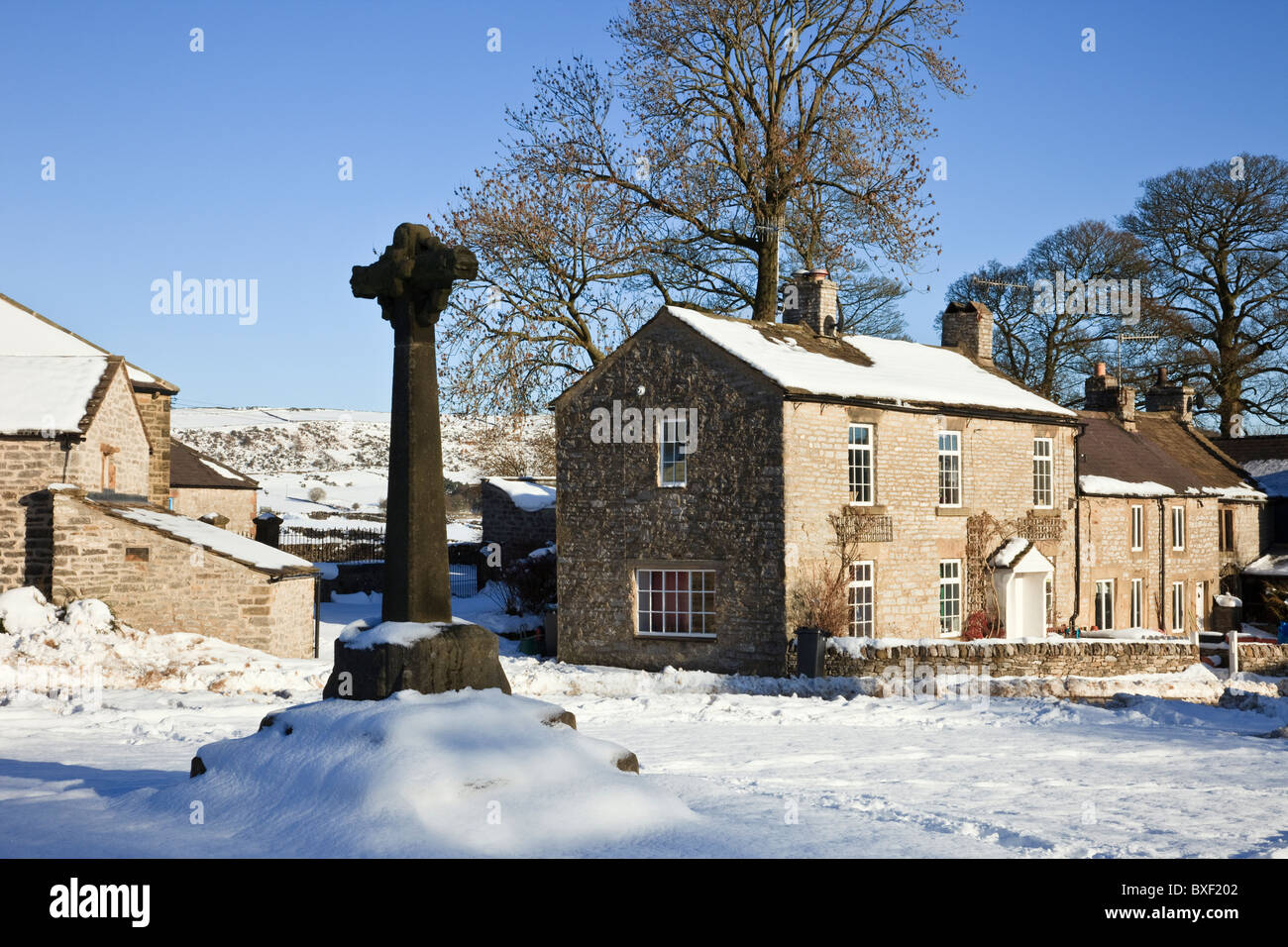 14th century carved stone cross in the Dovedale village green with snow in winter 2010. Foolow, Derbyshire, England, UK, Britain. Stock Photo