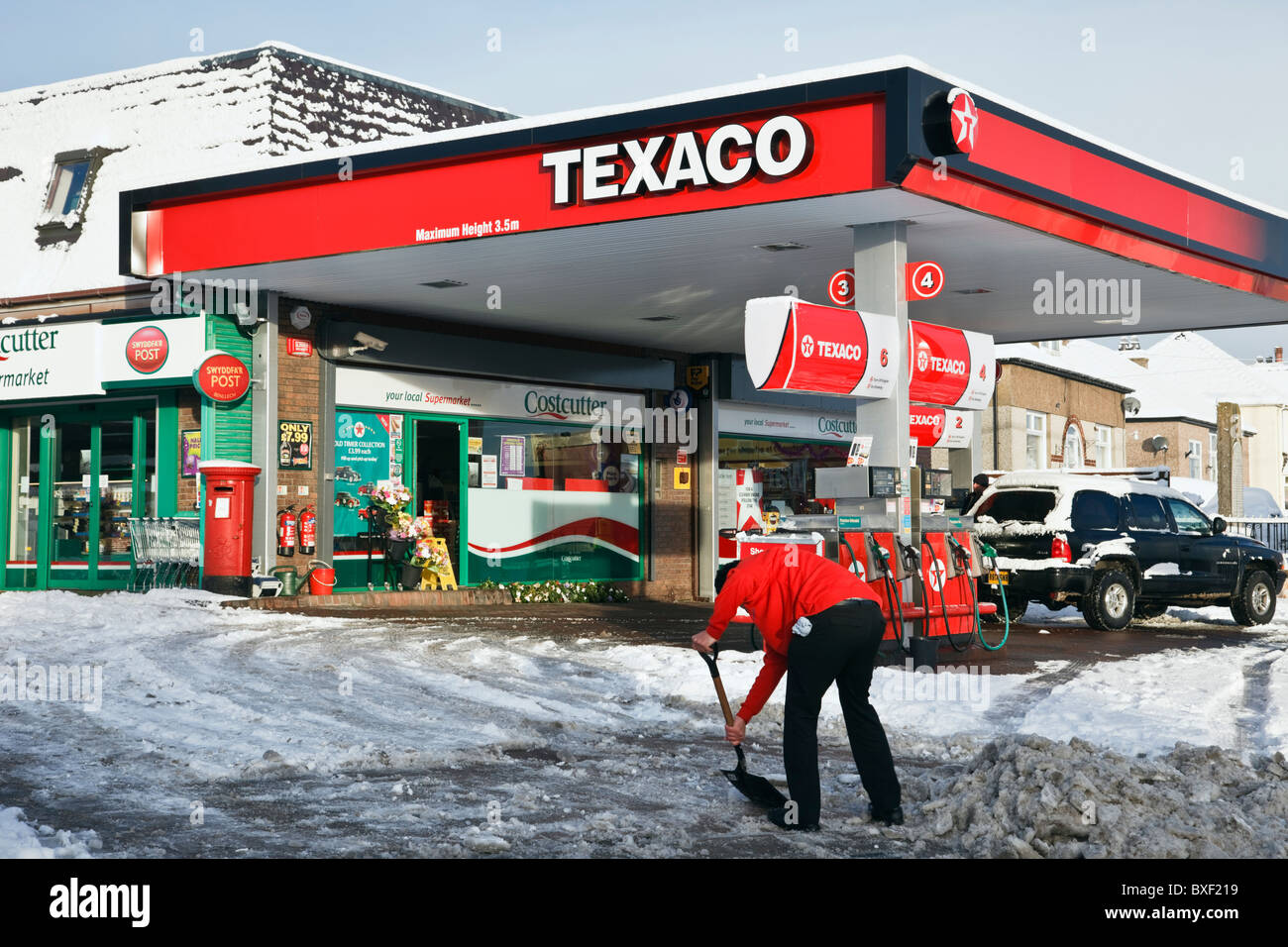 Man shovelling clearing snow from a Texaco petrol filling station forecourt after snowfall in bad winter weather. UK, Britain Stock Photo