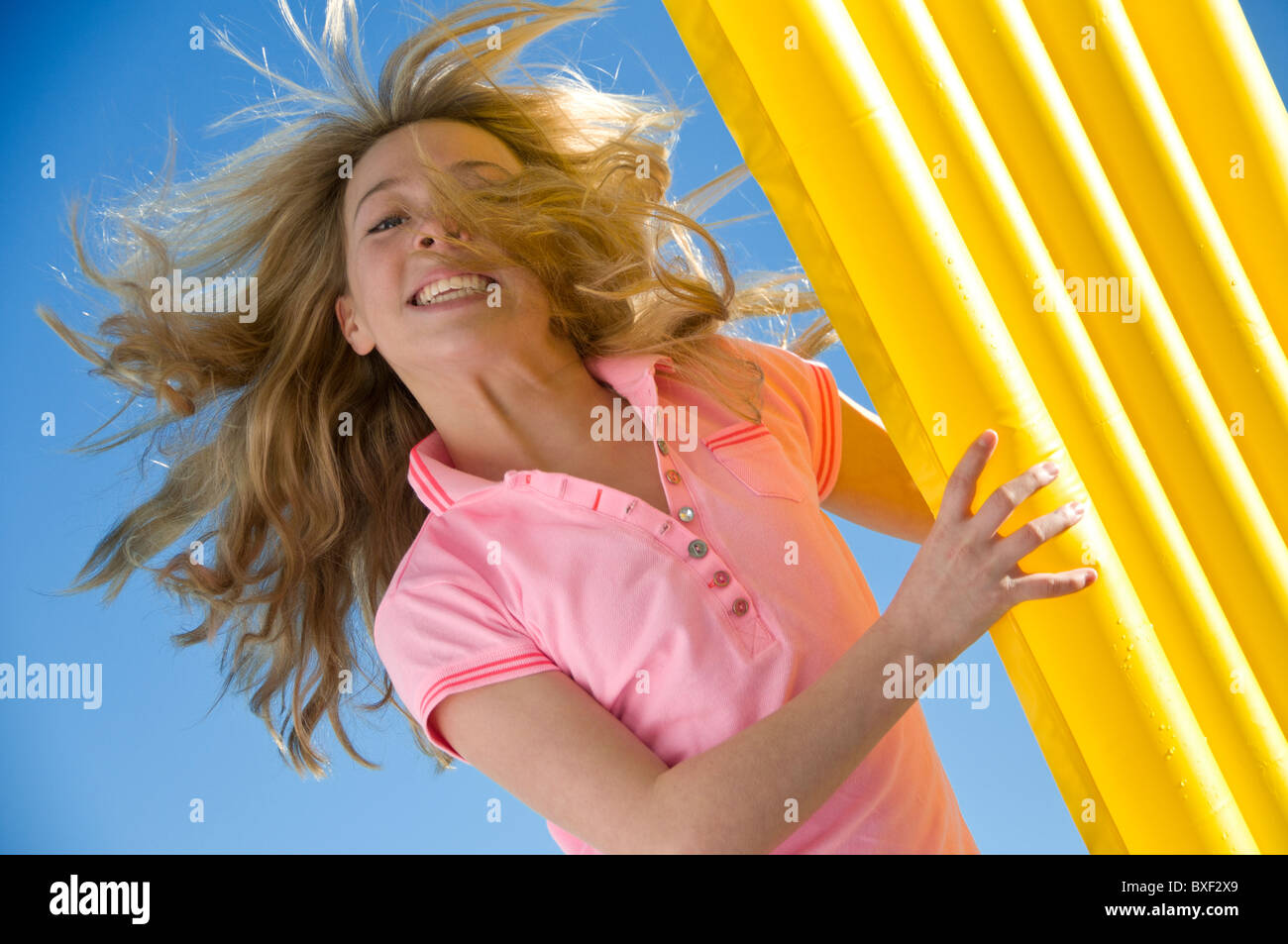 Fun Holiday Vibrant Action image attractive teenage girl 13-15 years with colourful floater lilo with hair blowing in sea breeze on vacation outdoors Stock Photo