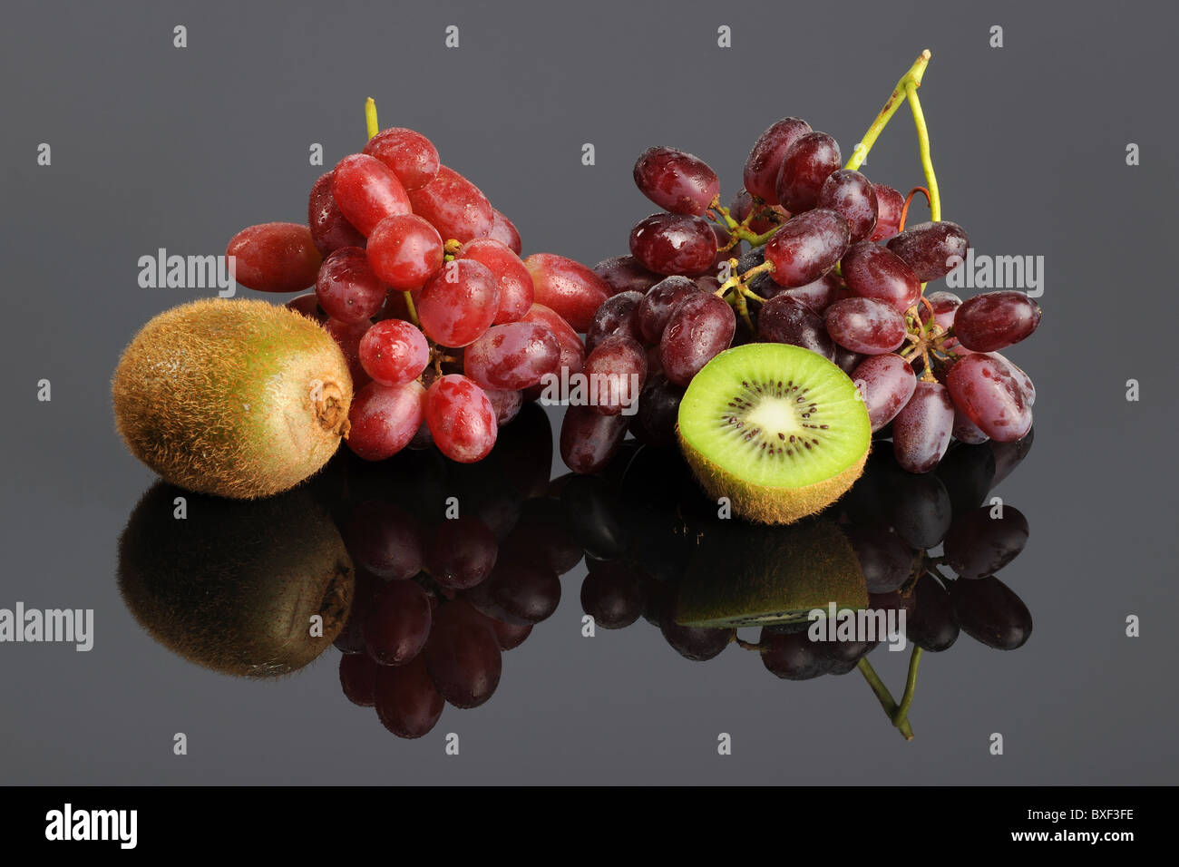 Red grapes and kiwi fruit over reflective table Stock Photo