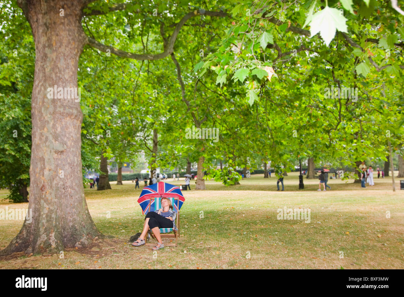 Woman asleep in a deckchair with a Union Jack umbrella. Photograph taken in Hyde Park. Stock Photo