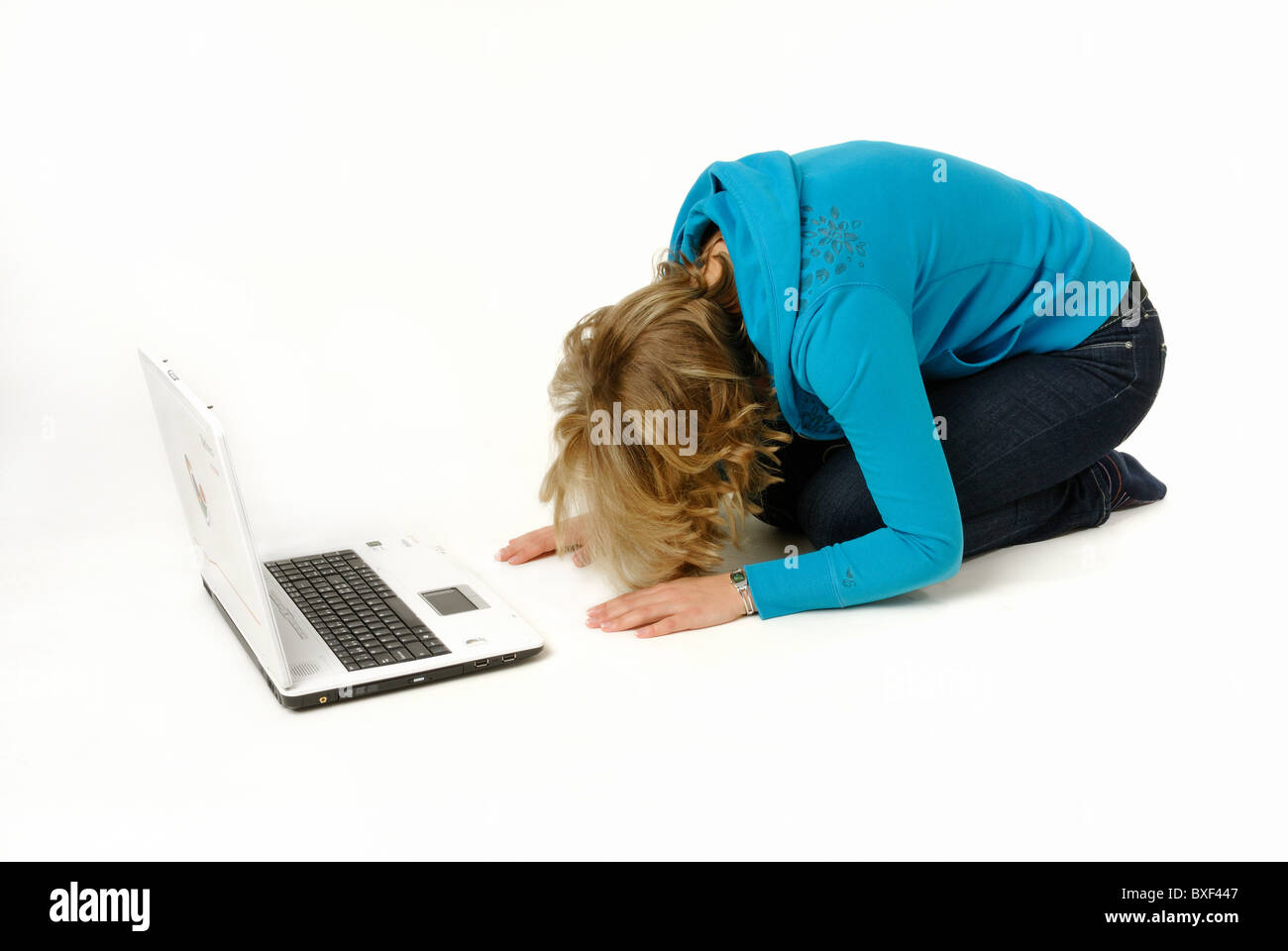 Young woman bowing in front of a laptop computer, worshipping the golden calf..... Stock Photo