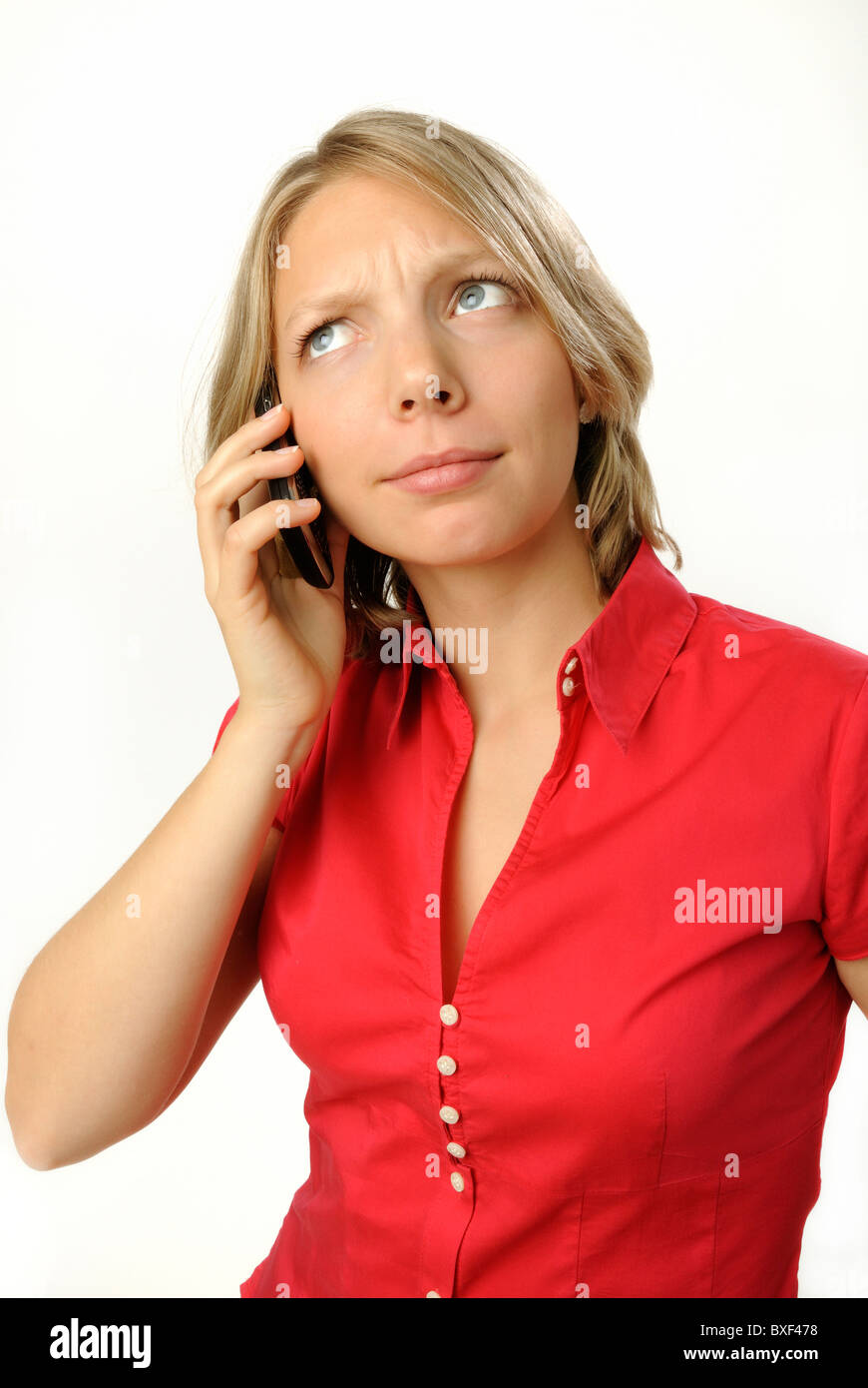Young woman in a red blouse making a call on a mobile phone, sceptical expression. Stock Photo