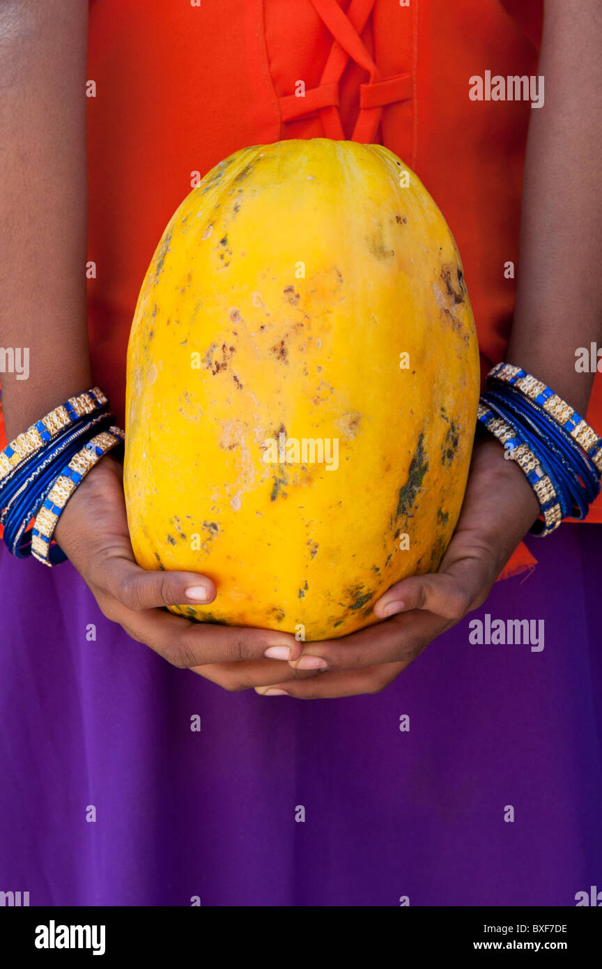 Indian girl holding a papaya behind her back. India Stock Photo