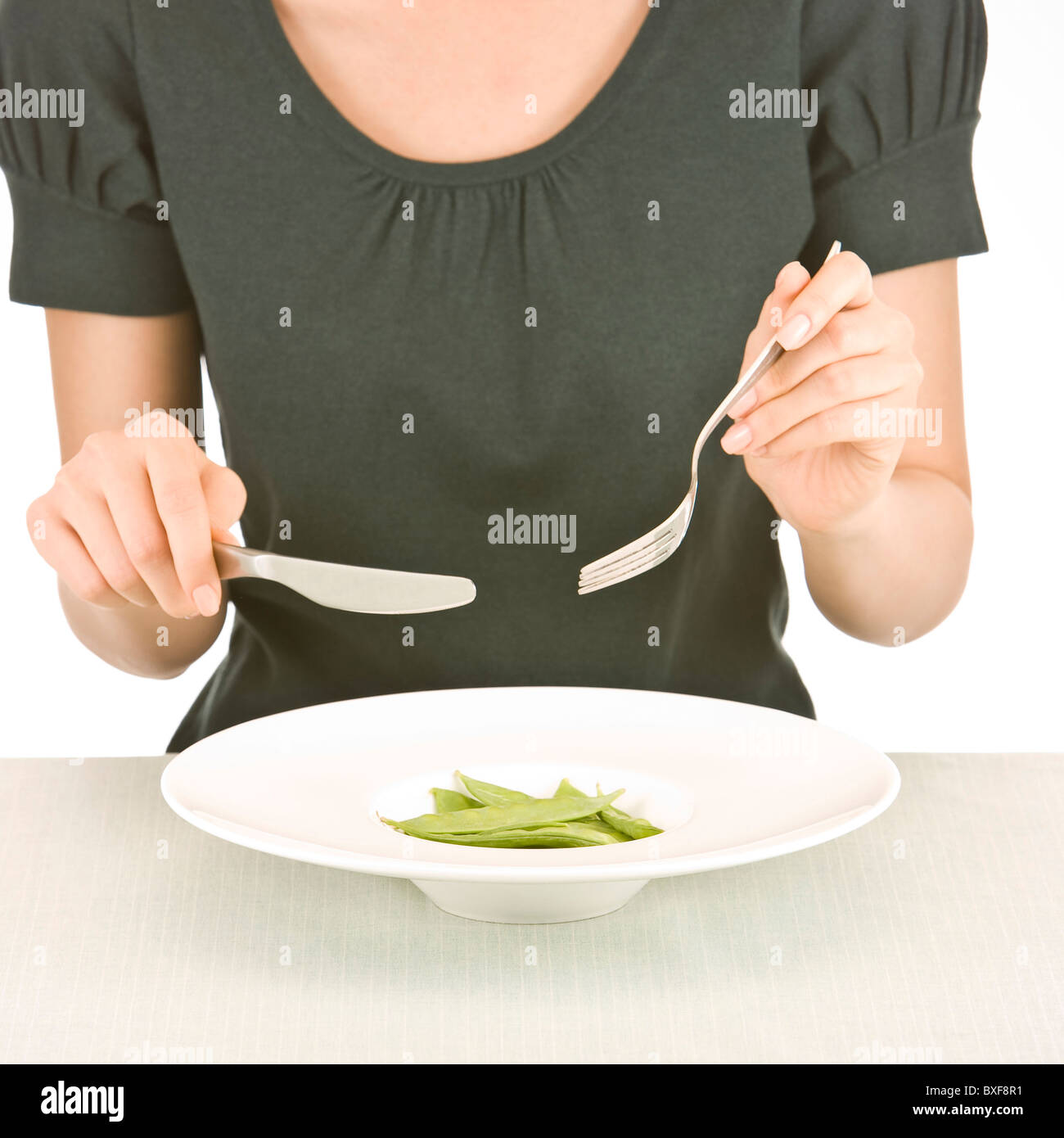 Woman sitting at table, holding fork and knife, close-up, mid section