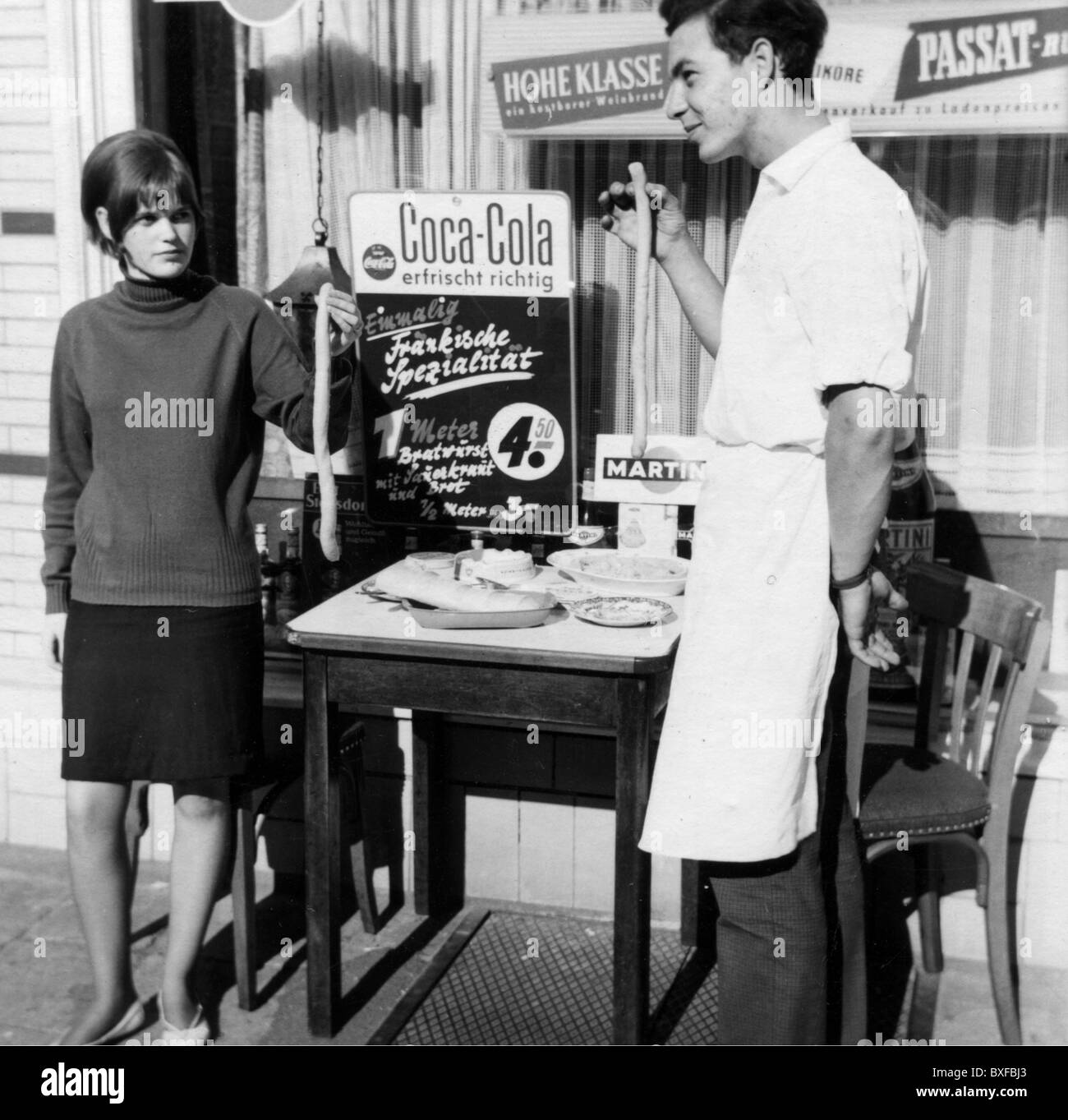 advertising, beverages, coke, a man and a woman presenting raw sausages in front of a shop window with a Coca Cola advertising sign, Germany, 1960s, Additional-Rights-Clearences-Not Available Stock Photo