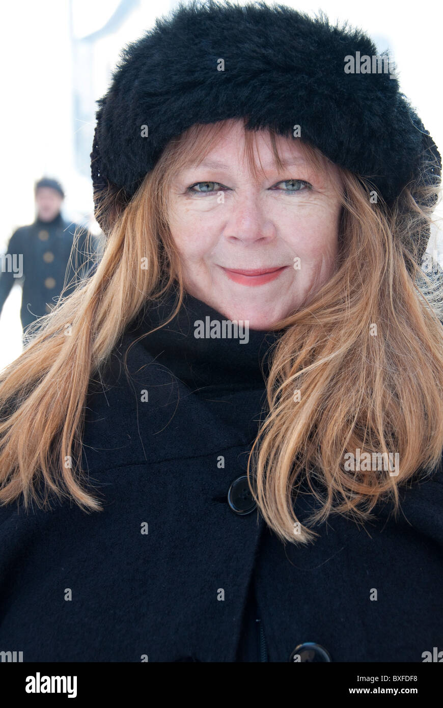 mature woman looking pleased in a black furn hat in the snow. Stock Photo