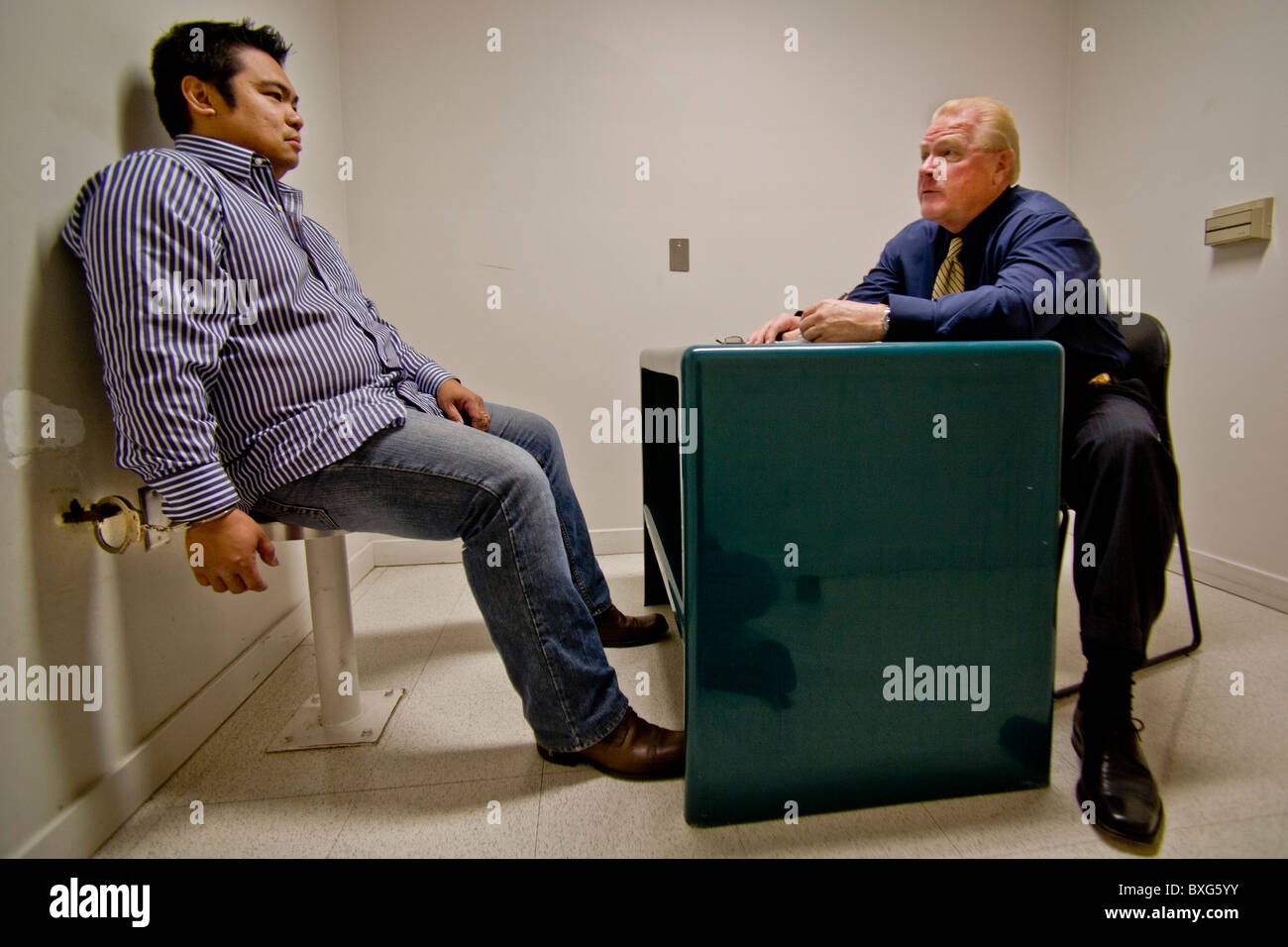 A handcuffed felony suspect is questioned by a Santa Ana, CA, police detective in a specialized interrogation room. Stock Photo