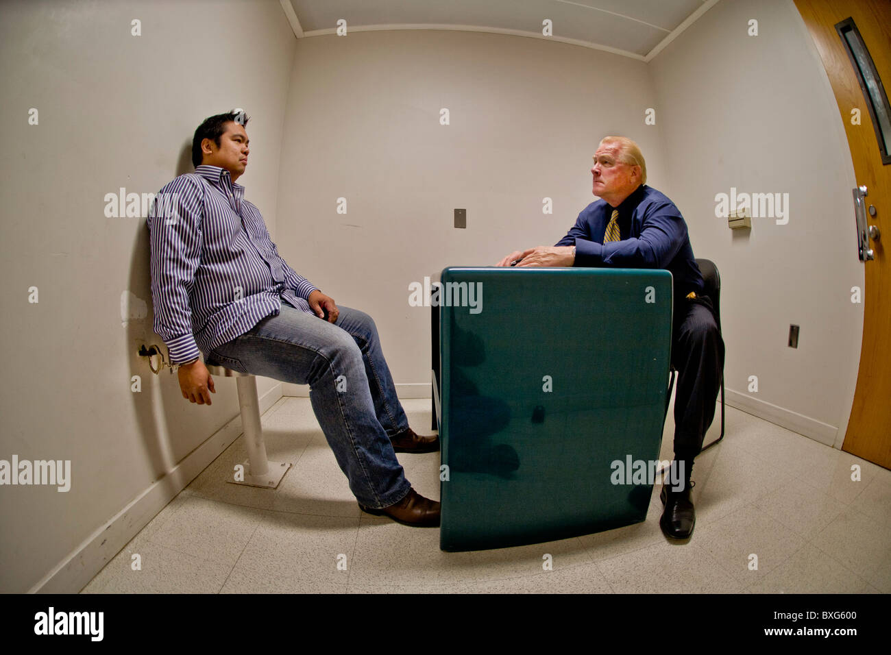 A handcuffed felony suspect is questioned by a Santa Ana, CA, police detective in a specialized interrogation room. Stock Photo