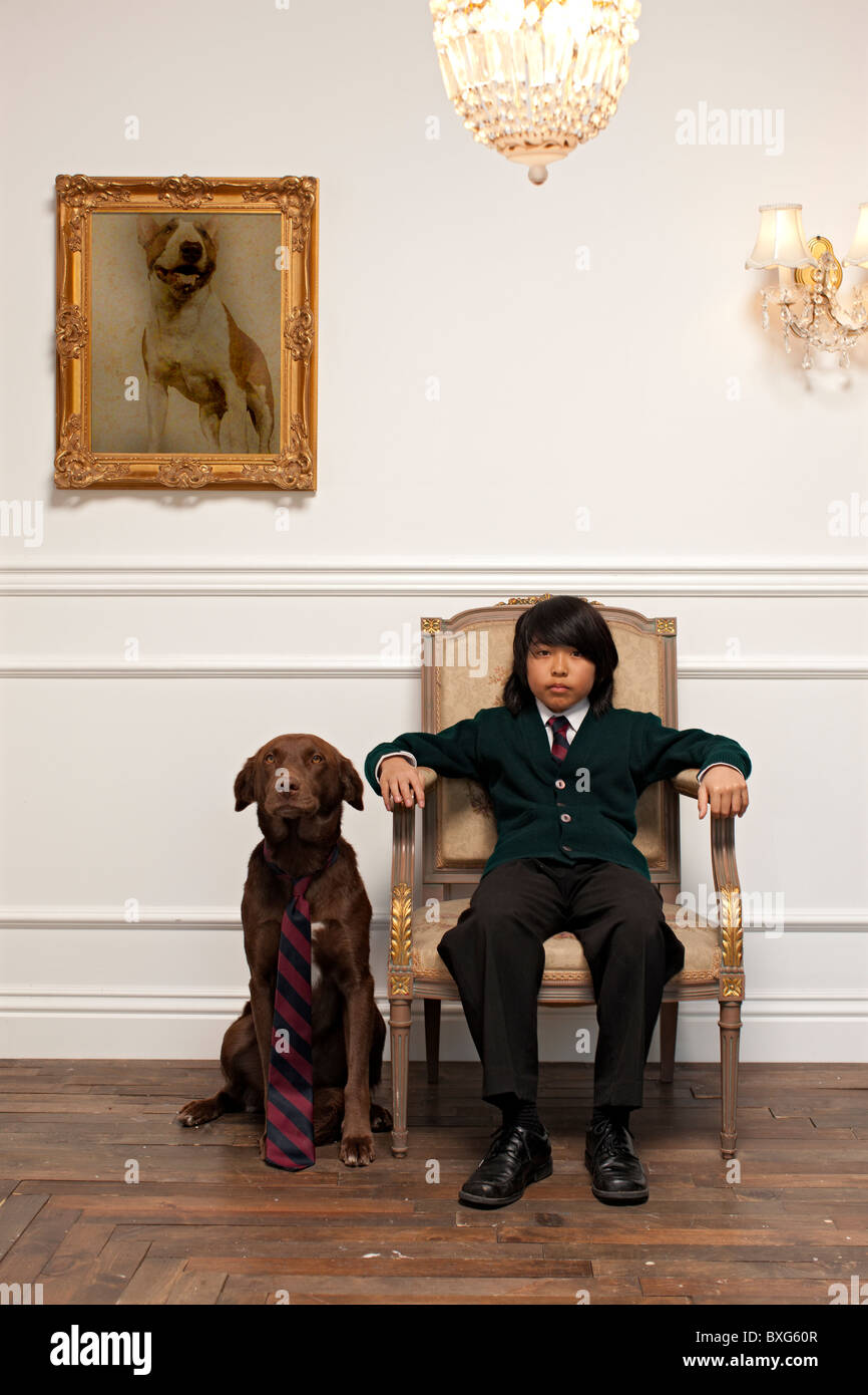 Vietnamese boy sitting on elegant chair next to dog with necktie Stock Photo