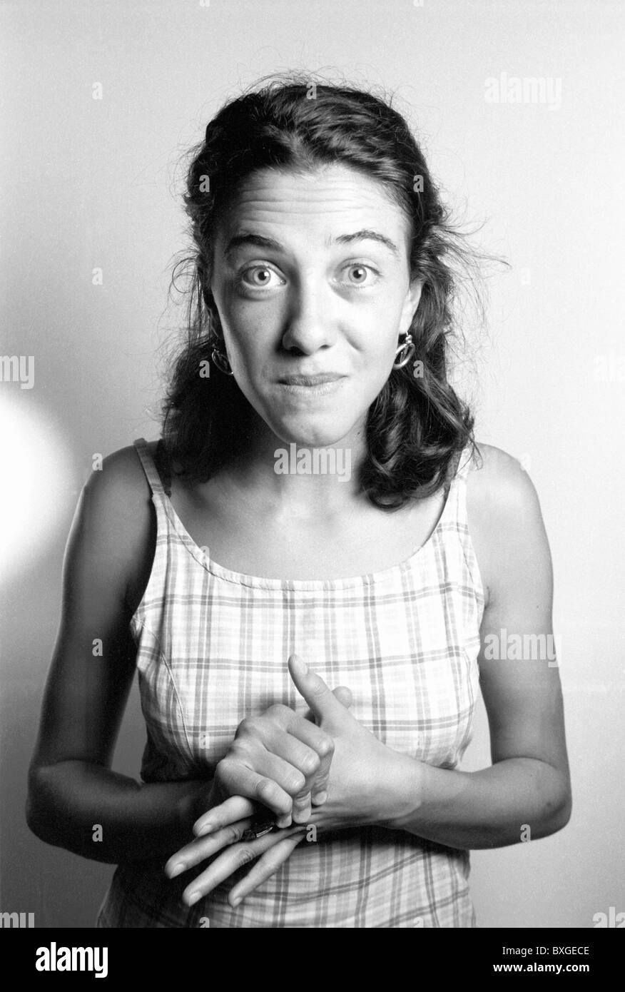 Young woman with hands clenched and looking anxiously at the camera. Stock Photo