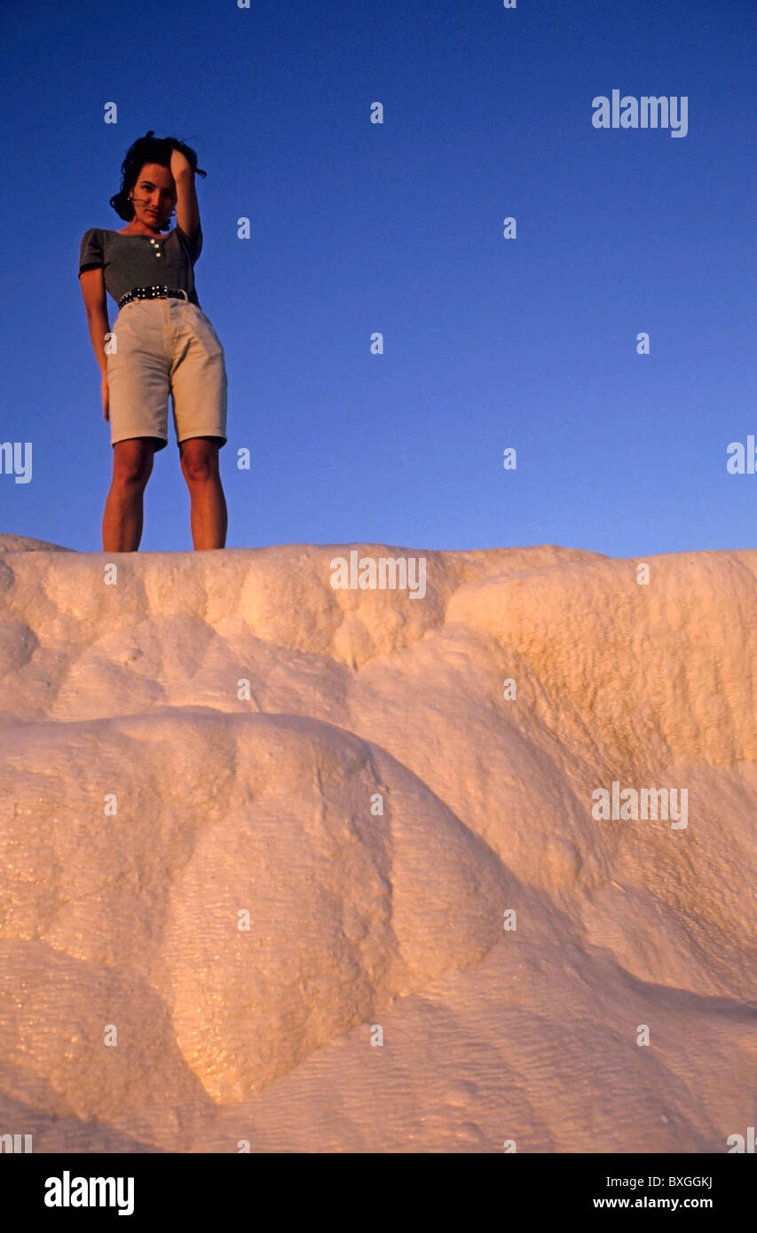 Young woman standing up on white rocks at sunset. Stock Photo