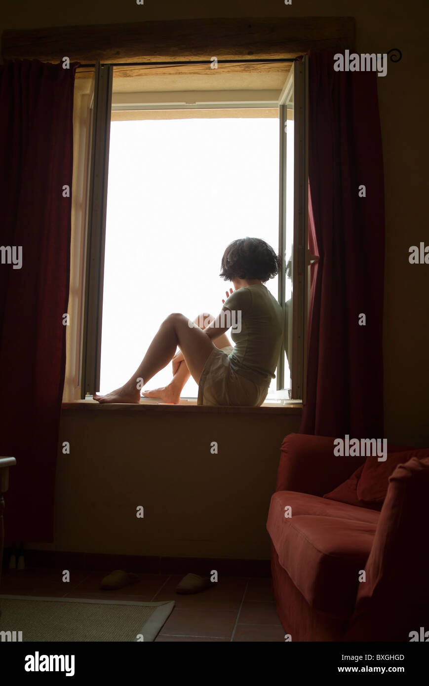 Woman silhouette sitting on her bedroom windowsill looking out and daydreaming Stock Photo