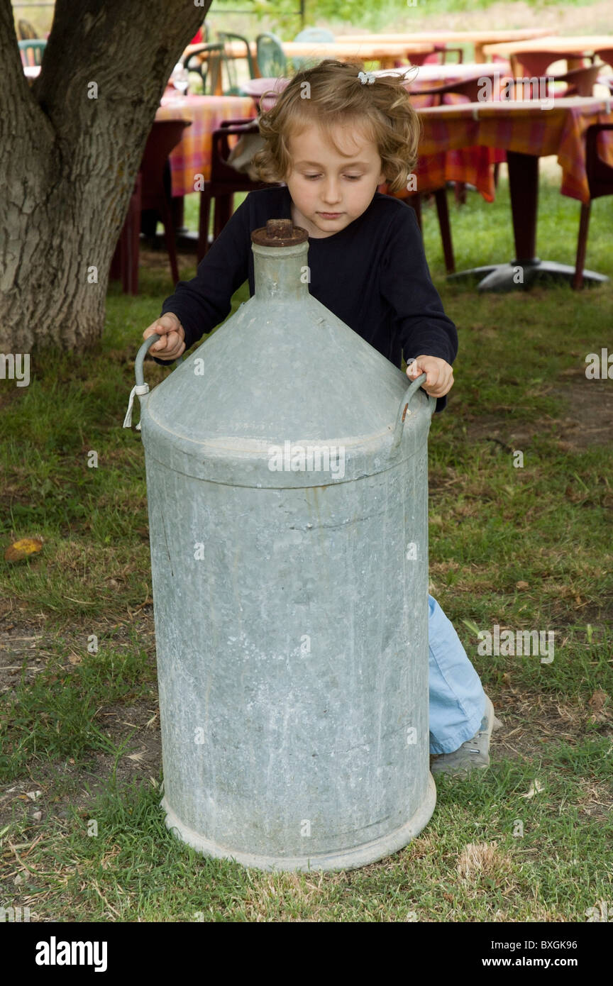 Little girl playing around an old milk urn, France. Stock Photo