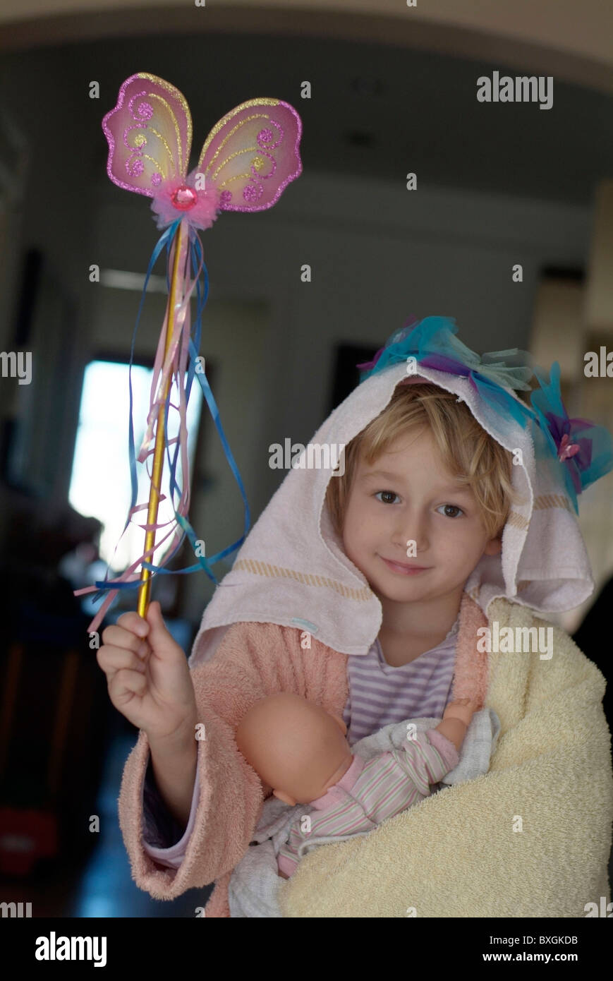 Little girl playing dress-up with a magic wand and baby doll. Stock Photo