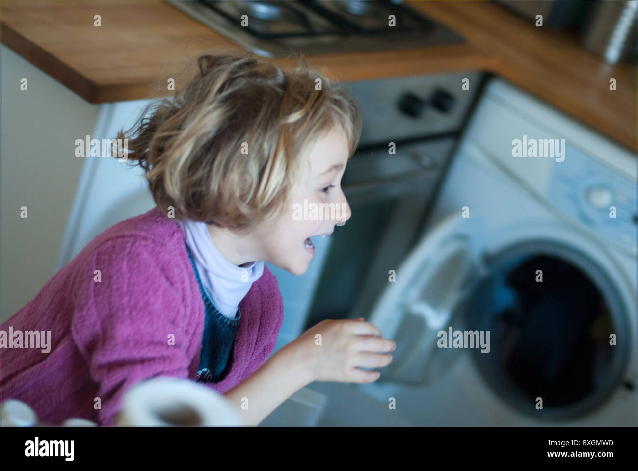 Little blond girl laughing and running around in the kitchen, France. Stock Photo