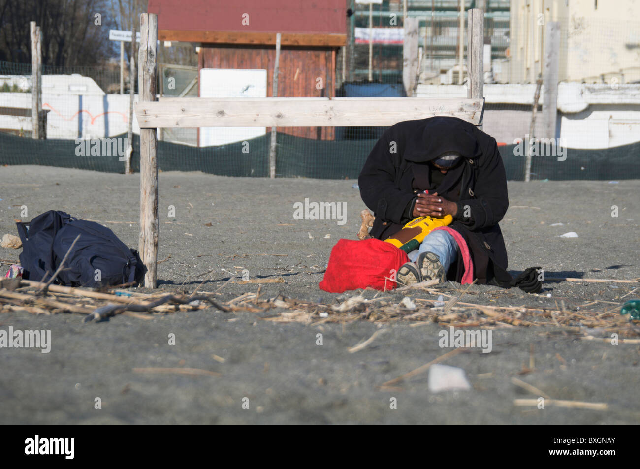 Ostia beach, black homeless man sleeps under sun on a cold winter afternoon Stock Photo