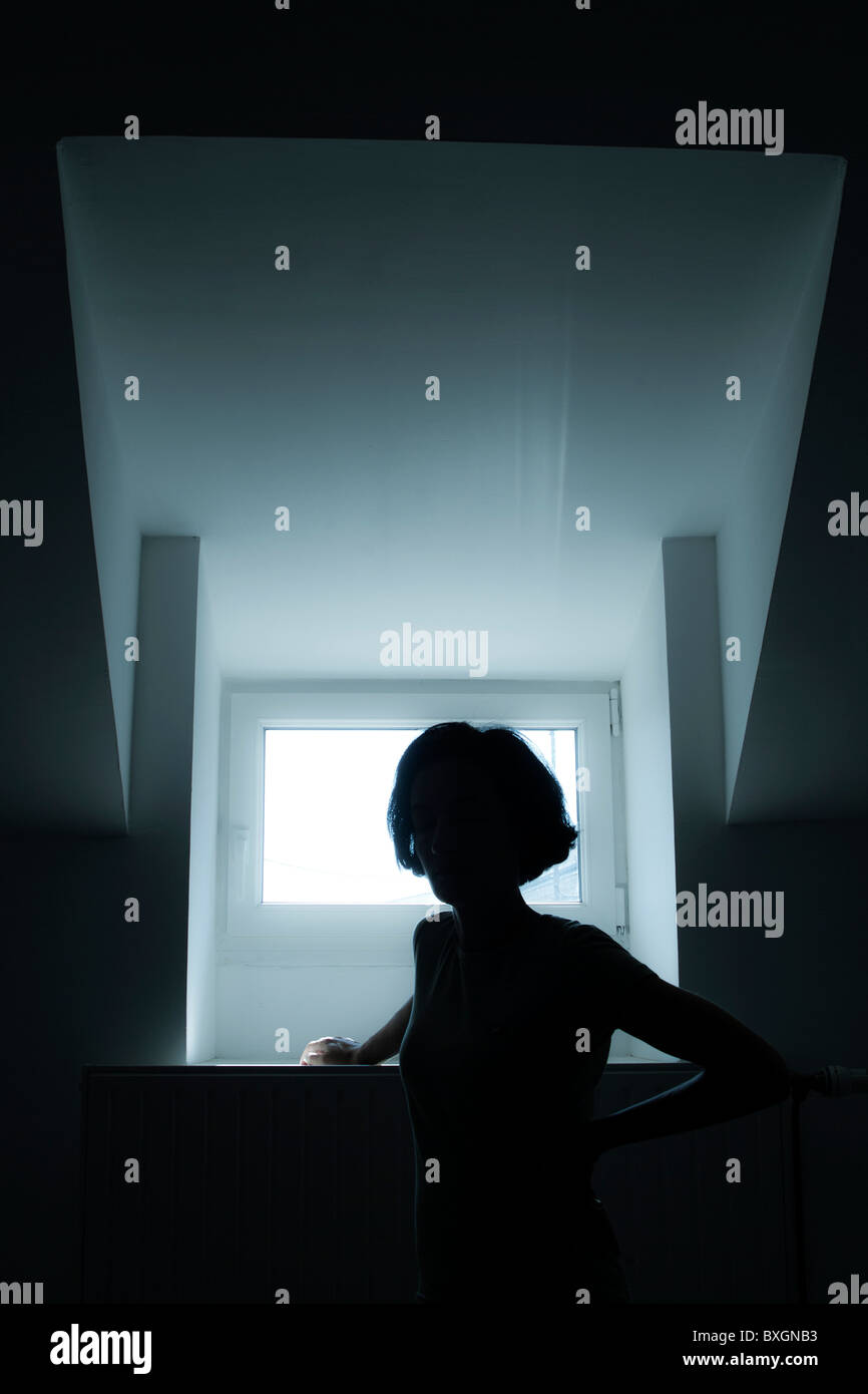 Silhouette of a lonely woman standing in front of a window. Stock Photo