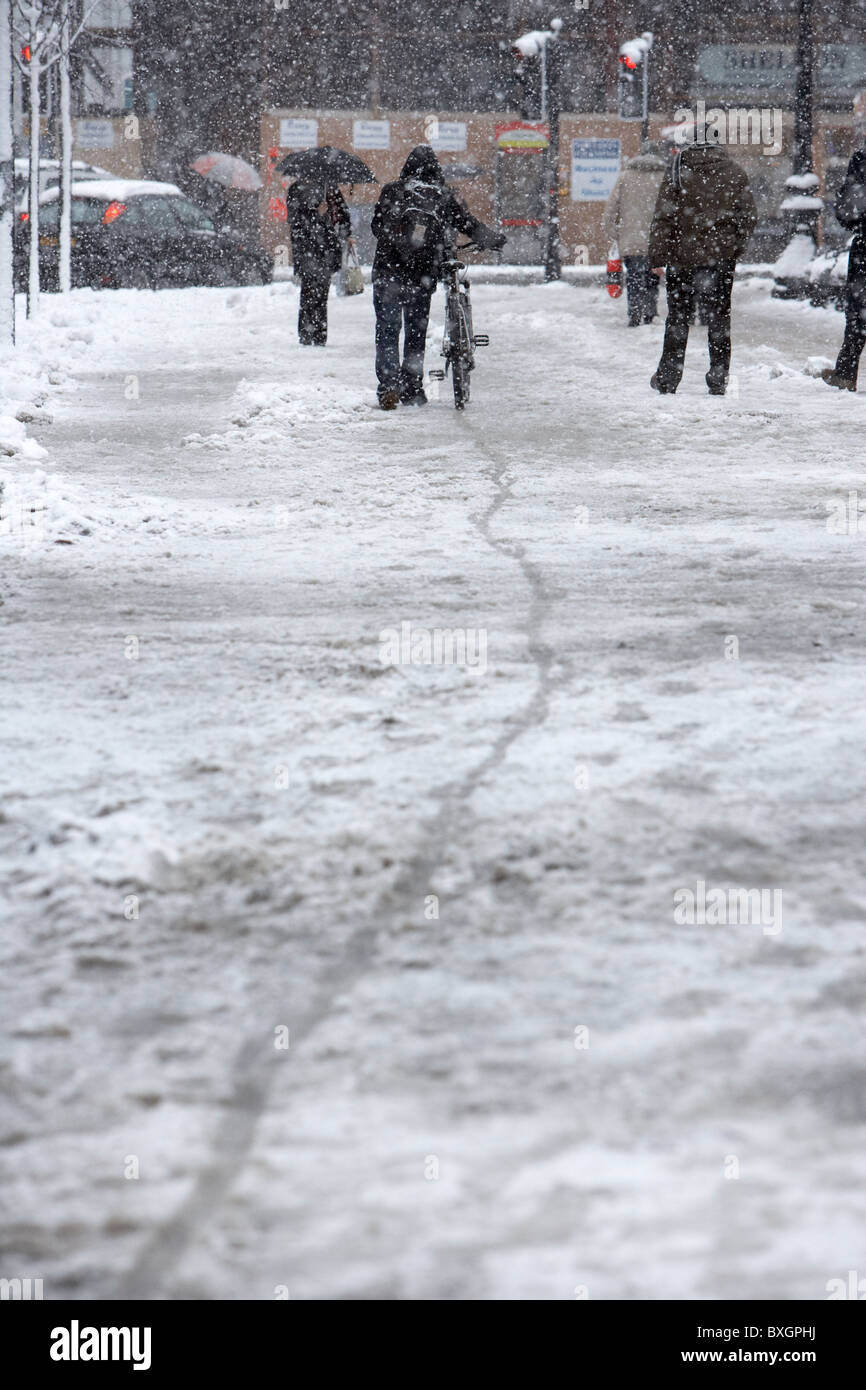 man walking bike through the snow on a cold snowy winters day Belfast Northern Ireland Stock Photo