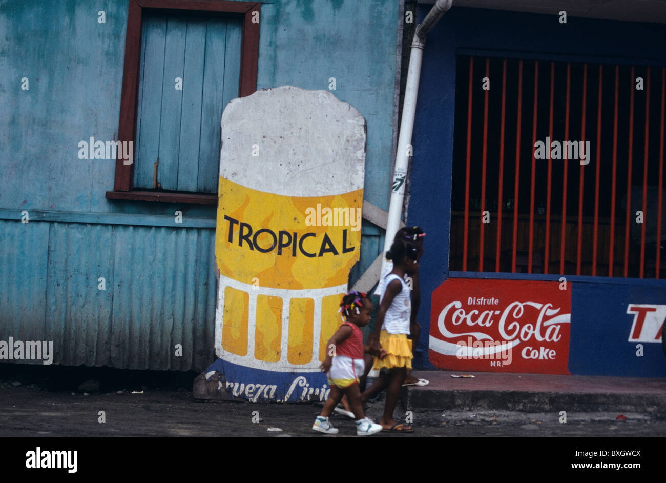 Costa Rica, Kleine Rasta Maedchen laufen vor bunter Werbung | Costa Rica, Little Rasta Girls passing by, coloured advertisement Stock Photo