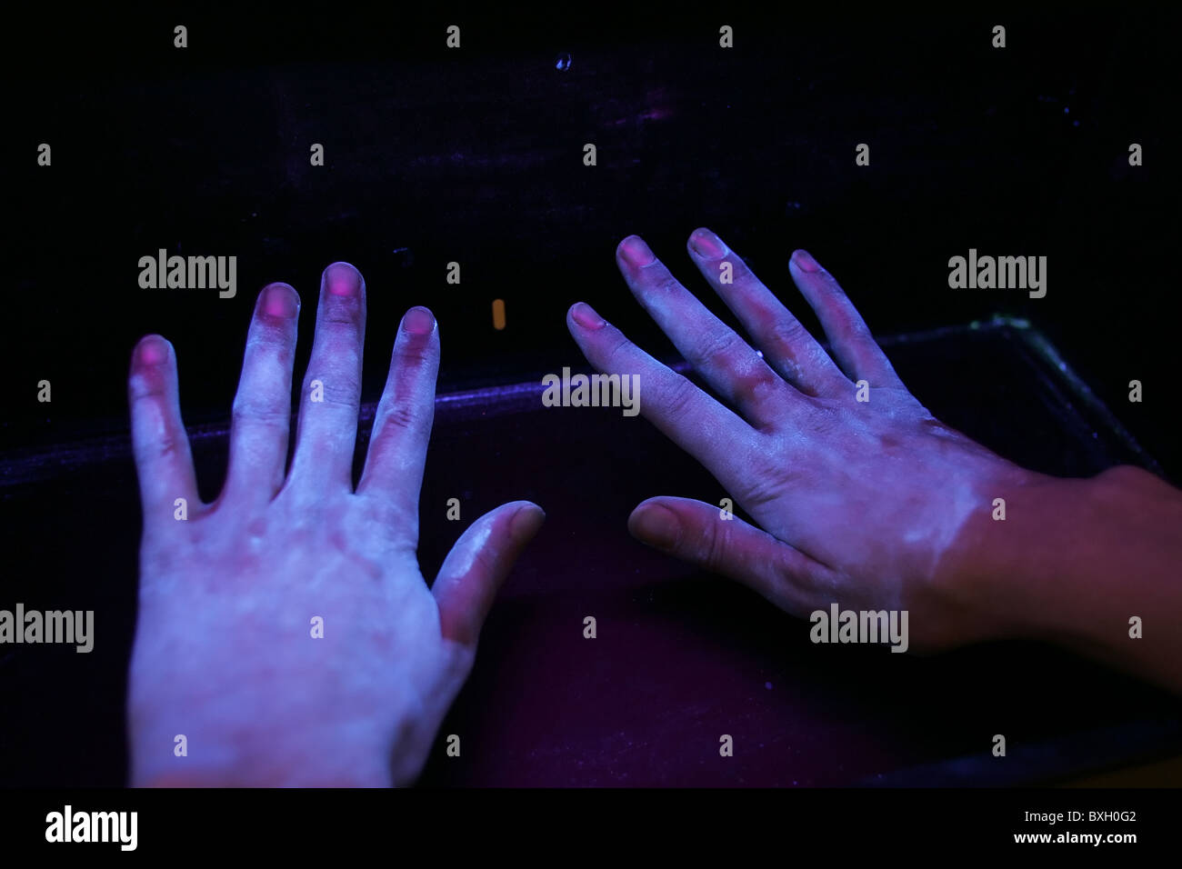 Hands placed under a UV light source indicate how effective normal hand-washing has been. Dark areas indicate missed areas. Stock Photo