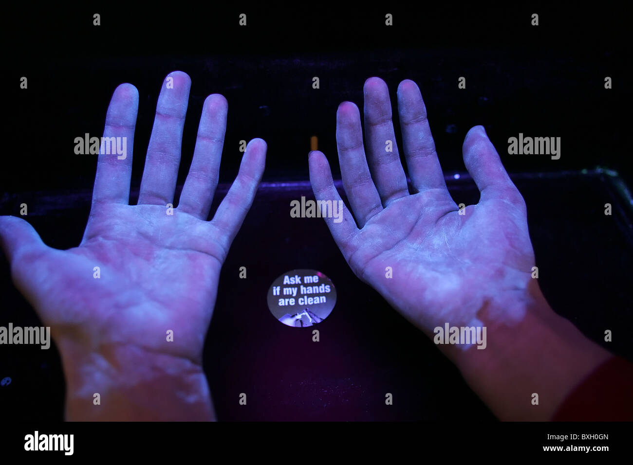 Hands placed under a UV light source indicate how effective normal hand-washing has been. Dark areas indicate missed areas. Stock Photo
