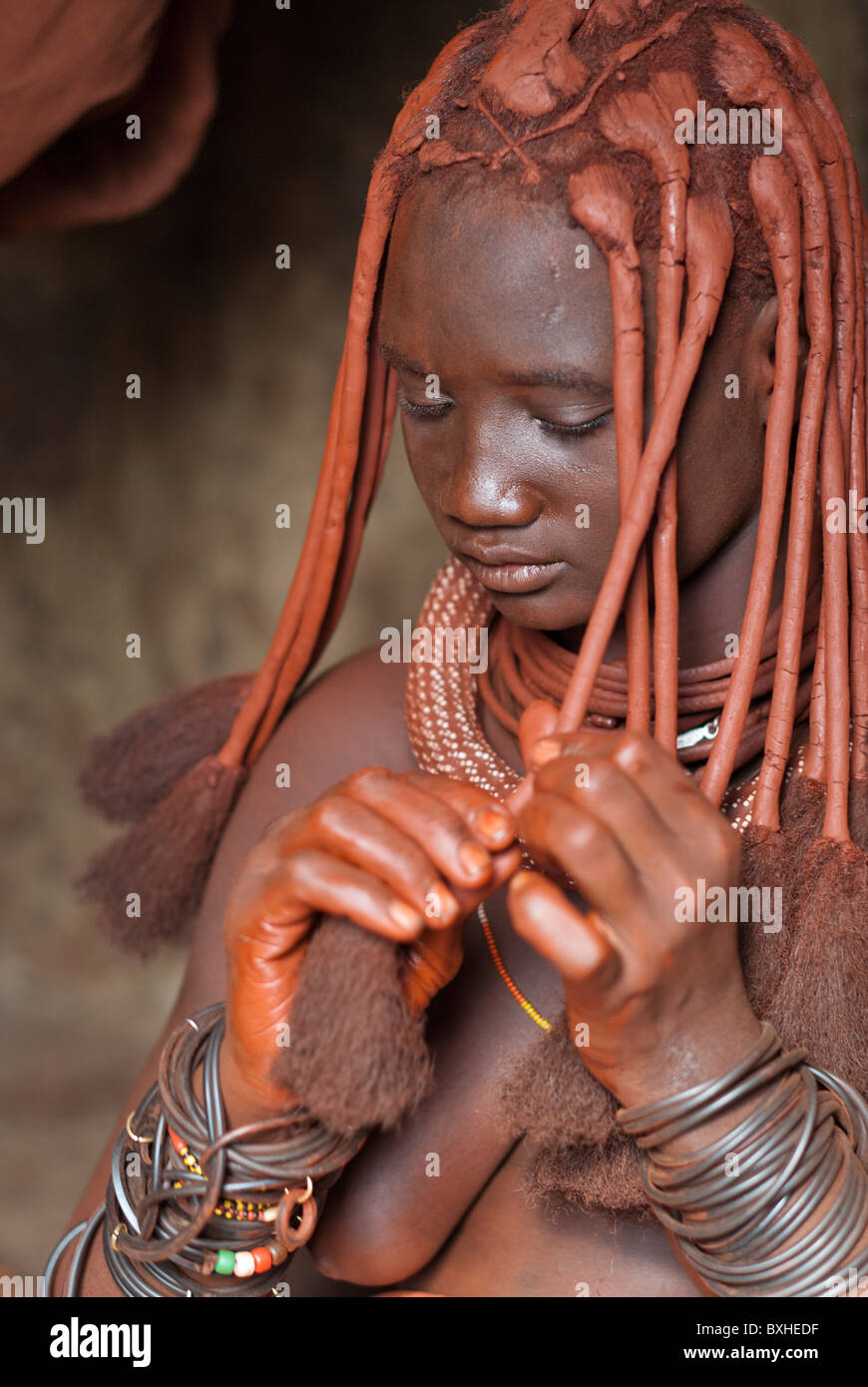 Himba woman in her hut styling her hairdo in a village near Epupa Falls, Namibia, Africa. Stock Photo