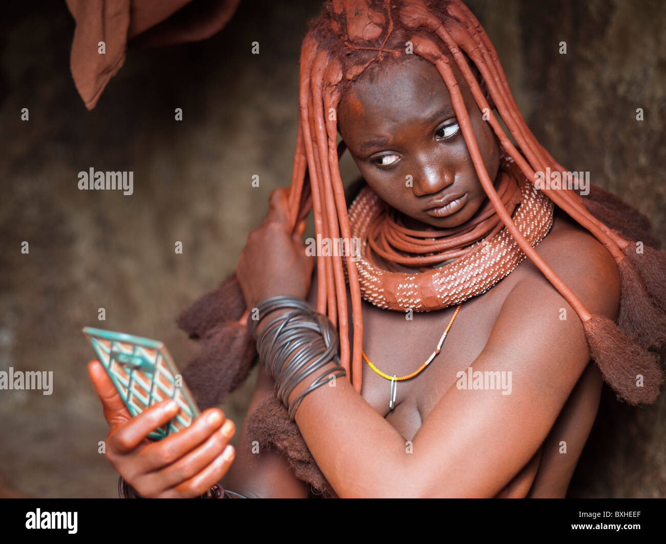 Himba woman in her hut styling her hairdo in a village near Epupa Falls, Namibia, Africa. Stock Photo