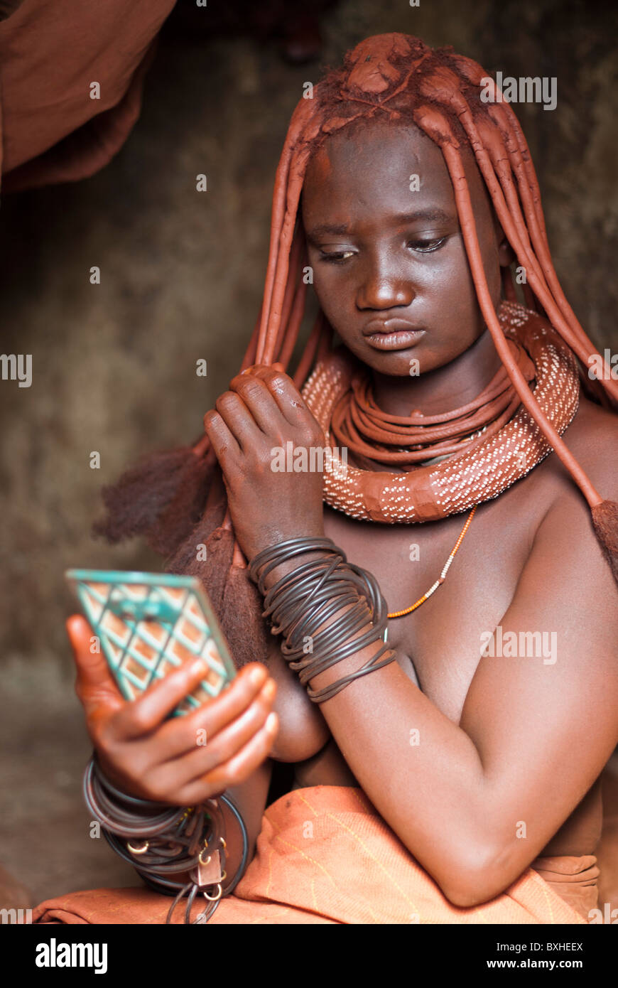 Himba woman in her hut styling her hairdo in a village near Epupa Falls, Namibia, Africa. Stock Photo