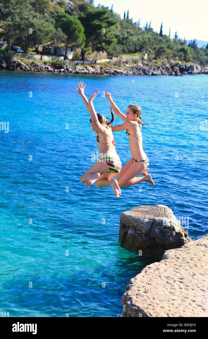 Children jump into the sea at Nissaki Beach, Corfu, Greece. No model release. Stock Photo