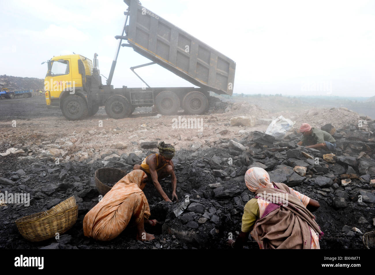 India Jharkhand Dhanbad Jharia, people pick coal at overburden dumping site of opencast mine of Bharat coking coal Ltd., behind Volvo truck of BCCL Stock Photo