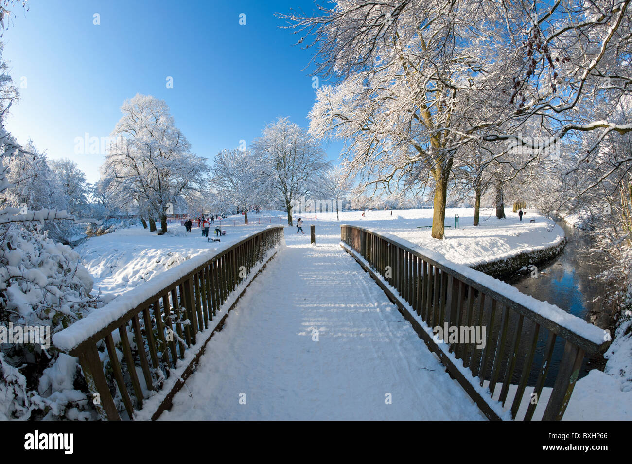 Winter snow scene in park land with trees, people and bridge Stock Photo