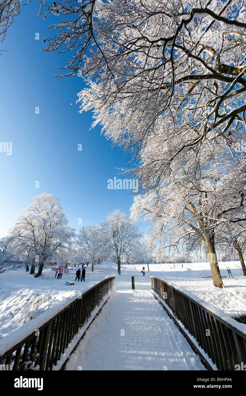 Winter snow scene in park land with trees, people and bridge Stock Photo