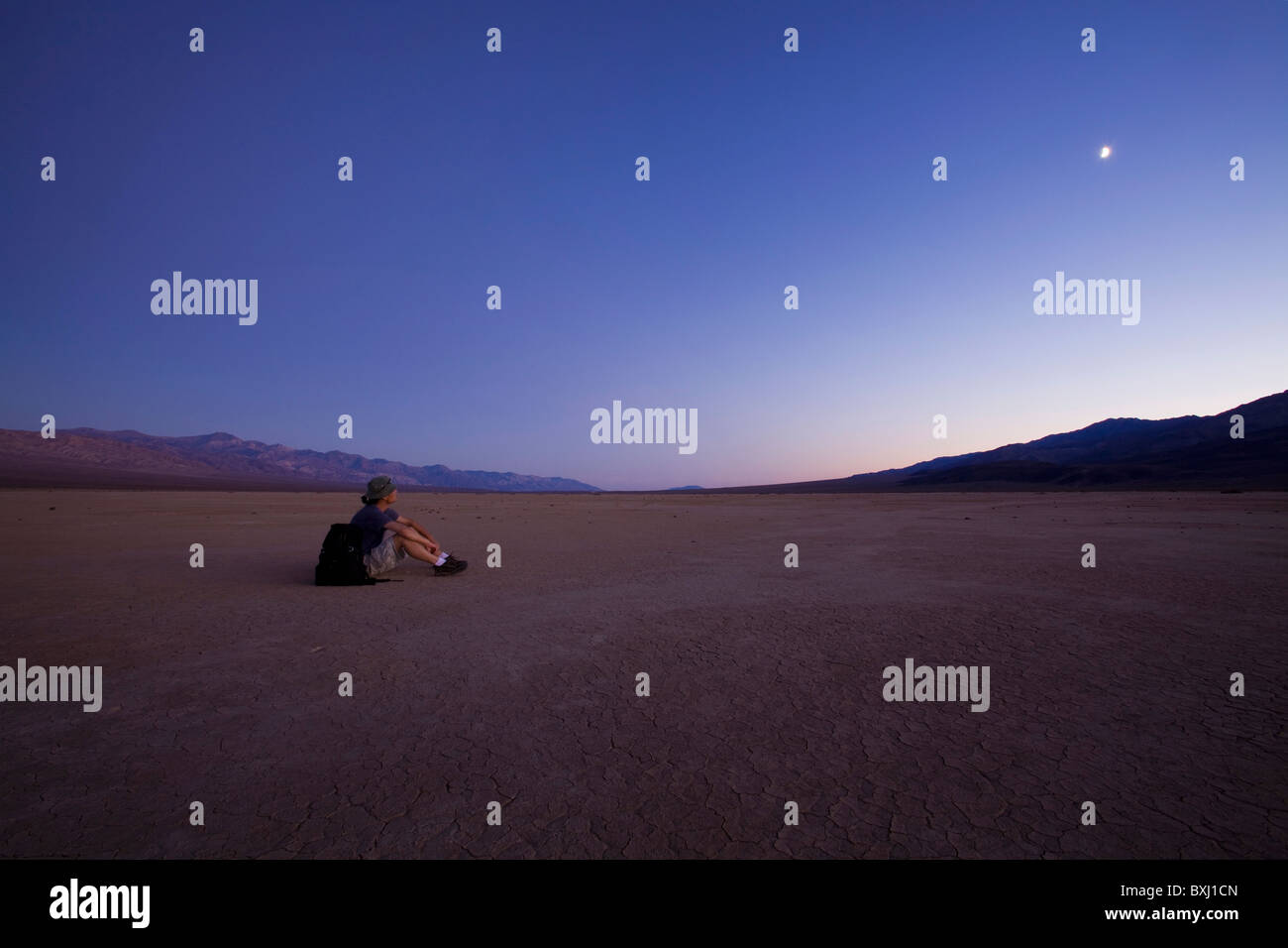 Man sits on moonlit dry lake bed - Death Valley, California, USA Stock Photo