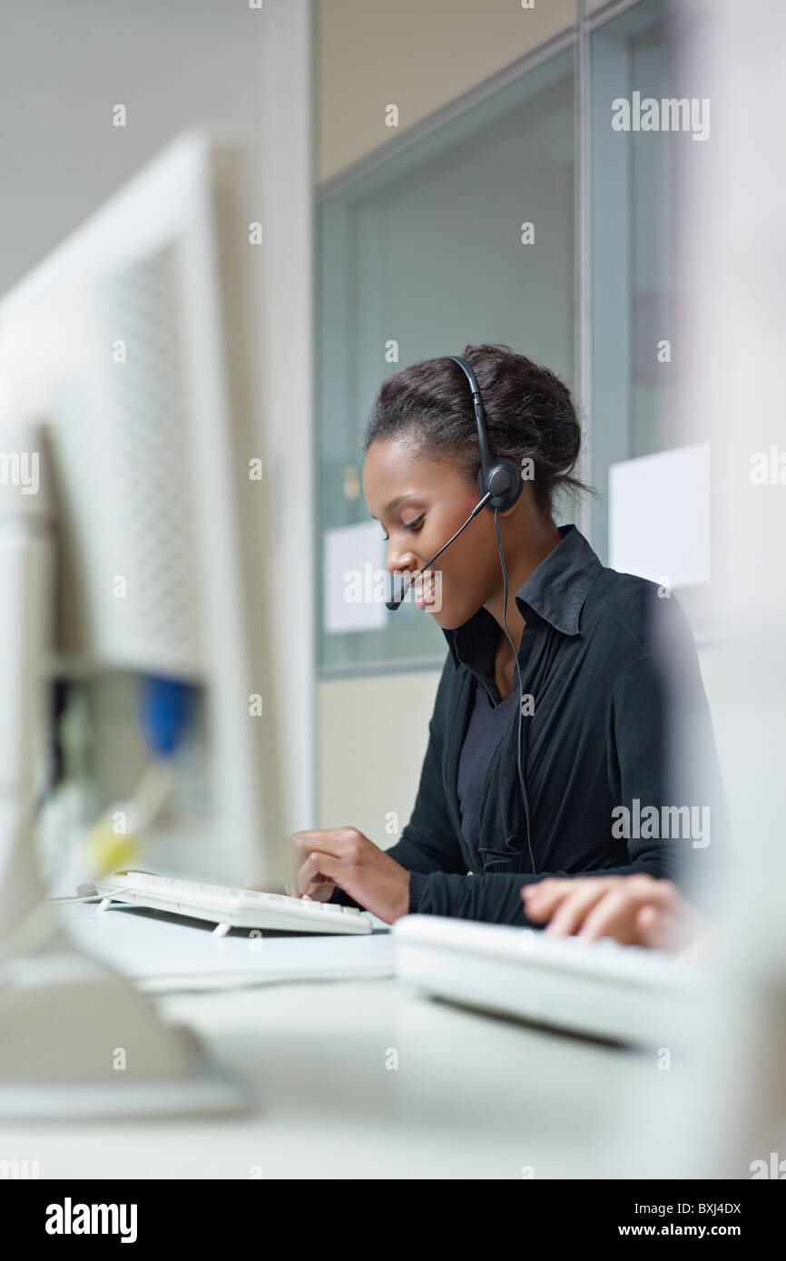 female african american customer service representative talking on the phone and typing on pc. Vertical shape, side view Stock Photo