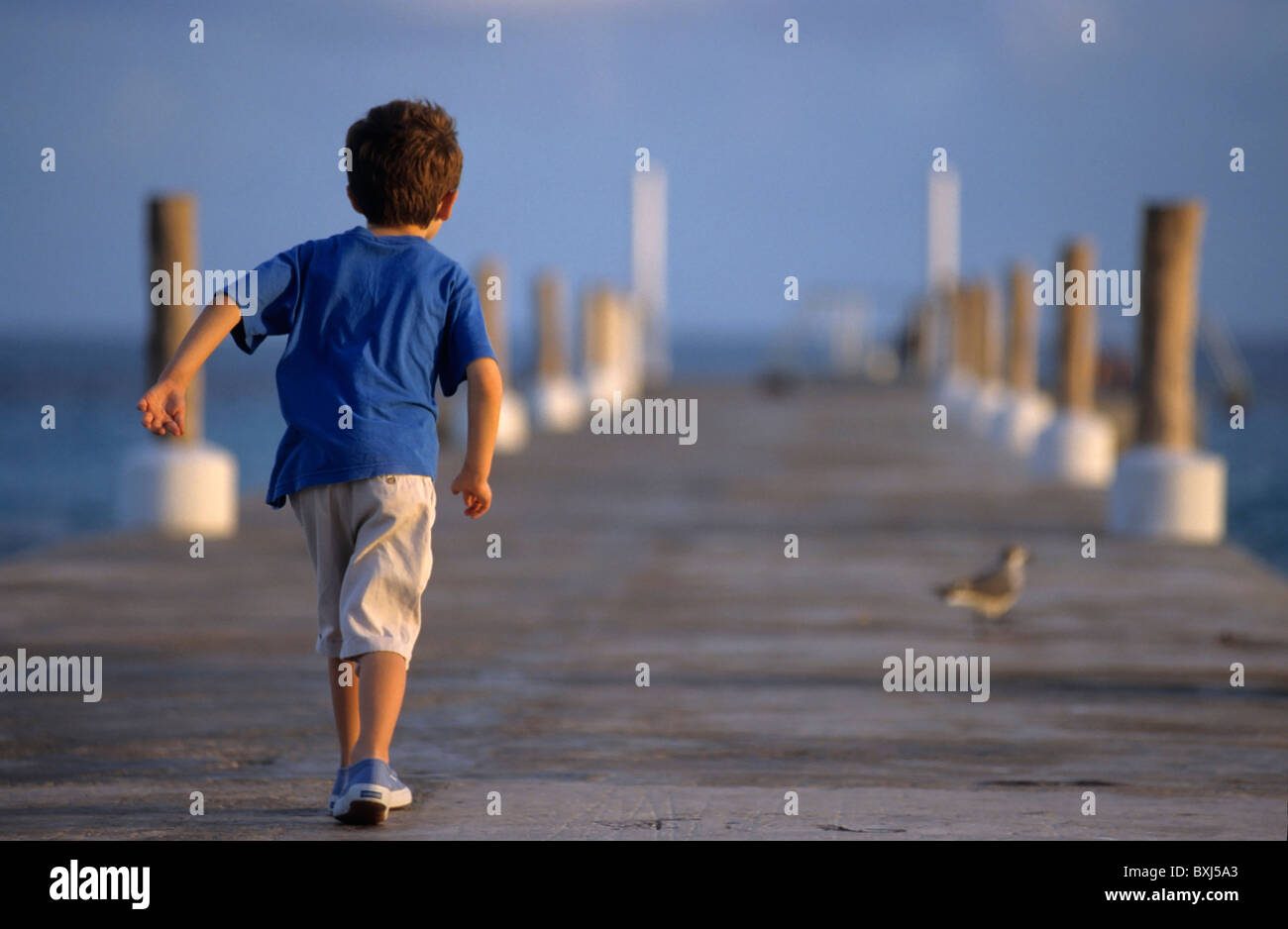Young boy walking on a wooden jetty at sunset in Cancún, Quintana Roo, Yucatán Peninsula, Mexico. Stock Photo