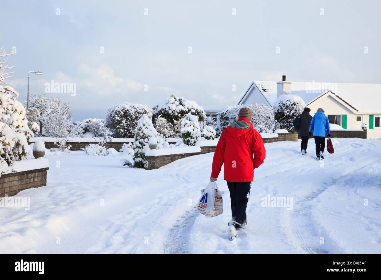 Snow scene with people carrying shopping along residential street on a