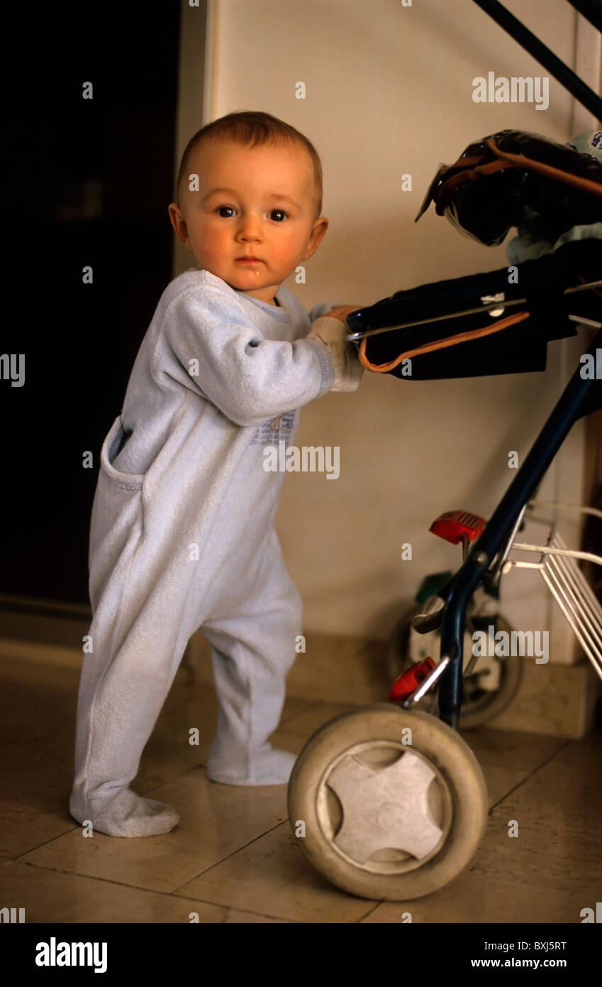 Baby girl learning to walk by pushing her baby stroller Stock